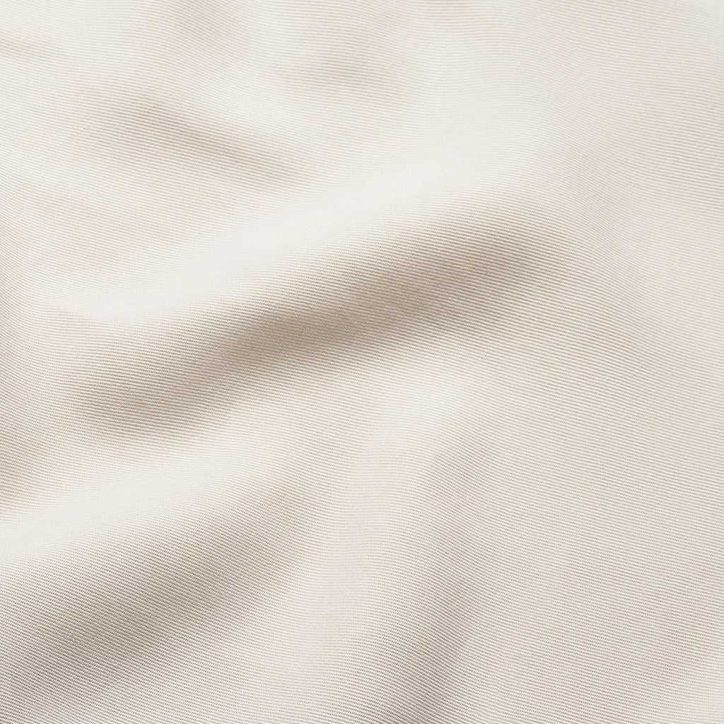 A close-up view of the Women's Cozy Earth Coastal Comfort Wrap Dress from Cozy Earth reveals a beige fabric with a soft, slightly wavy texture and subtle horizontal lines. The neutral tone and fine weave suggest a smooth and delicate material, indicative of high-quality cotton or linen. |Color:Sand