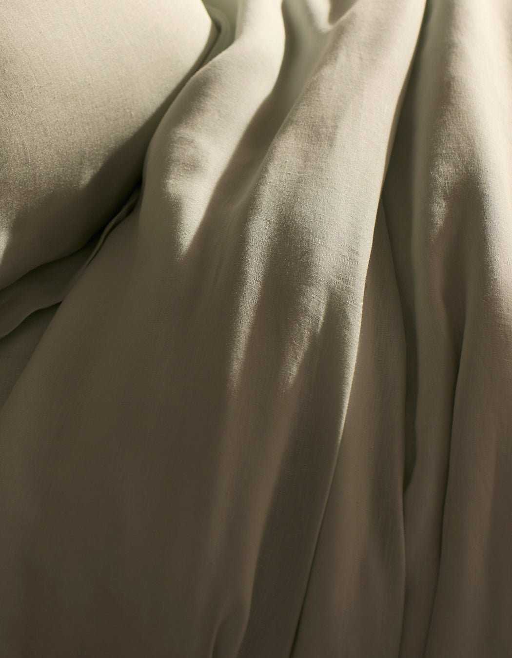 A close-up of Cozy Earth’s Linen Duvet Cover shows soft, beige fabric with gentle folds and a smooth, slightly wrinkled texture, creating a calm and cozy atmosphere—perfect for a relaxing bedroom.|Color:Mist