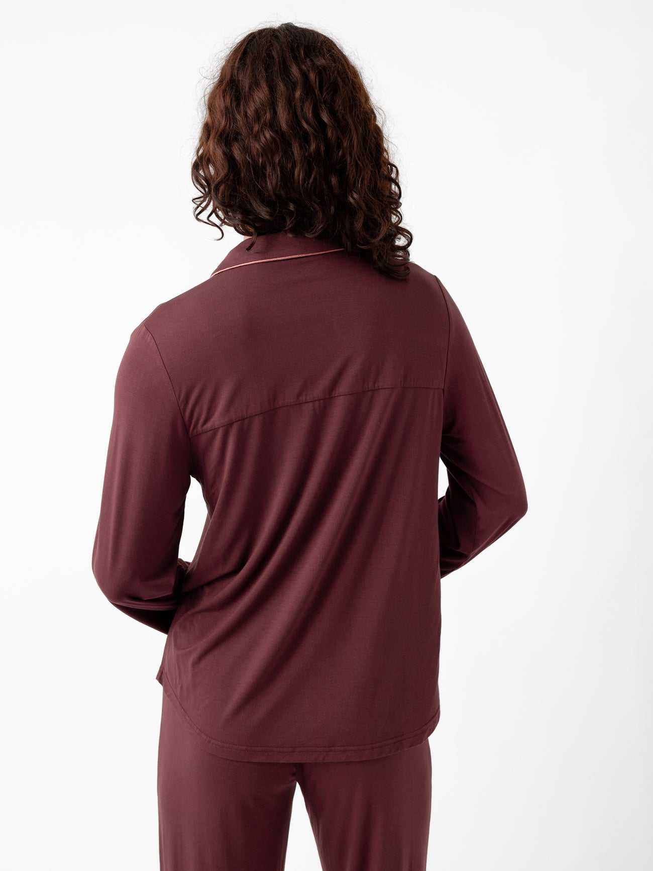 Rear view of a person with long curly hair wearing the Last Chance Women's Bamboo Stretch-Knit Pajama Set by Cozy Earth, featuring a maroon long-sleeve top and pants, against a plain white background. |Color:Burgundy