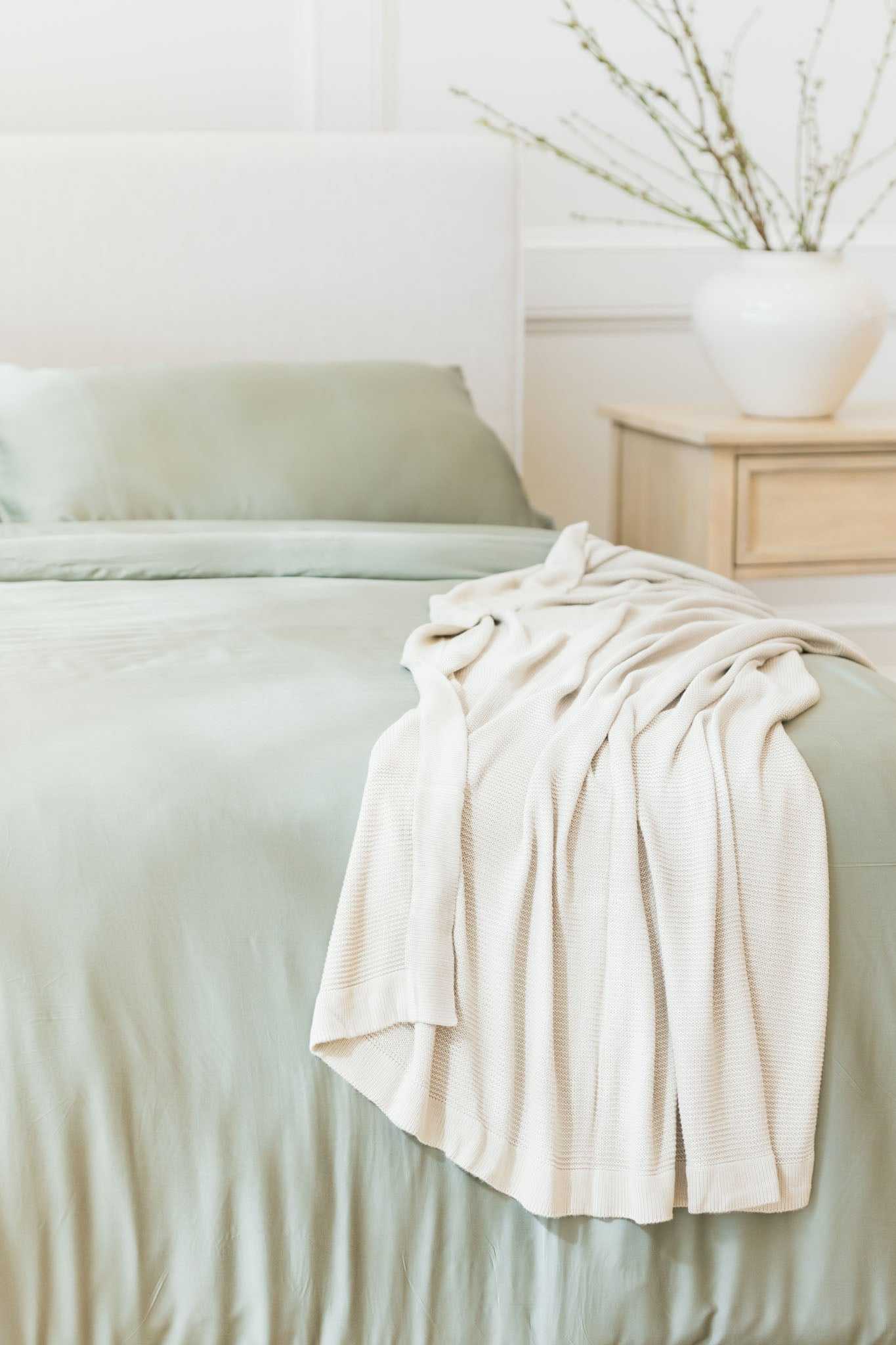 Driftwood cloud knit blanket draped over bed with sage sheets |Color:Driftwood