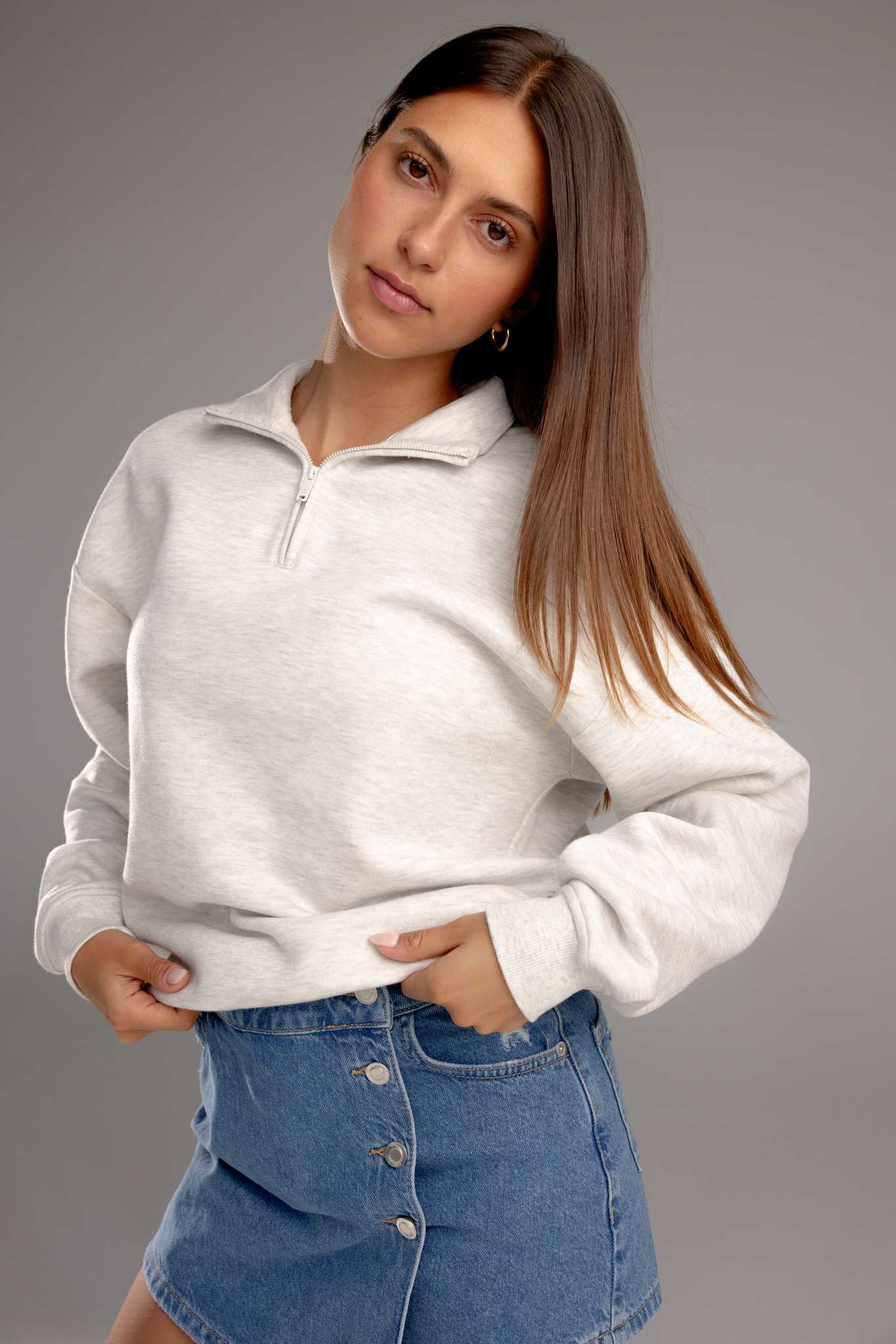 Heather Grey CityScape Quarter Zip. The quarter zip is being worn by a female model. The model is wearing an accompanying jean skirt to complete the look of the quarter zip. The photo was taken with a grey background. |Color:Heather Grey