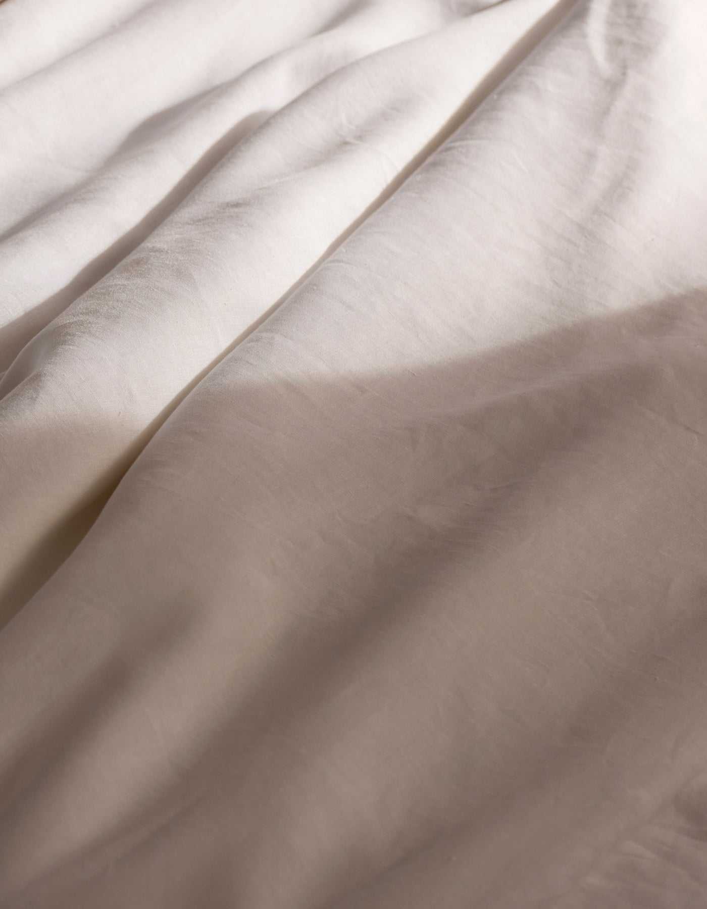 Soft sunlight casts gentle shadows across the Cozy Earth Linen Duvet Cover, its light-hued fabric creating a calm and cozy atmosphere.|Color:White