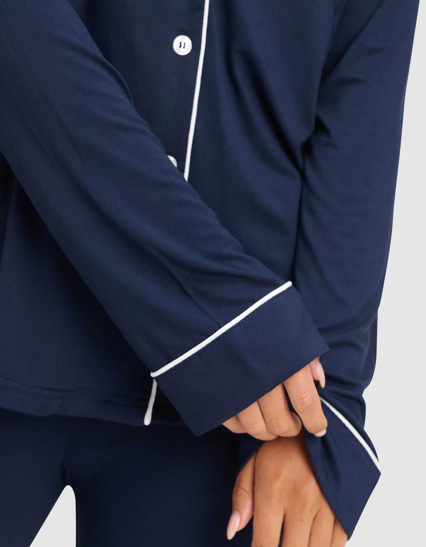 A woman models the Cozy Earth Women's Bamboo Stretch-Knit Long Sleeve Pajama Top in navy with white piping, shown from the shoulders down as she pulls at her sleeve. Only her lower body and hands are partially visible. |Color:Navy