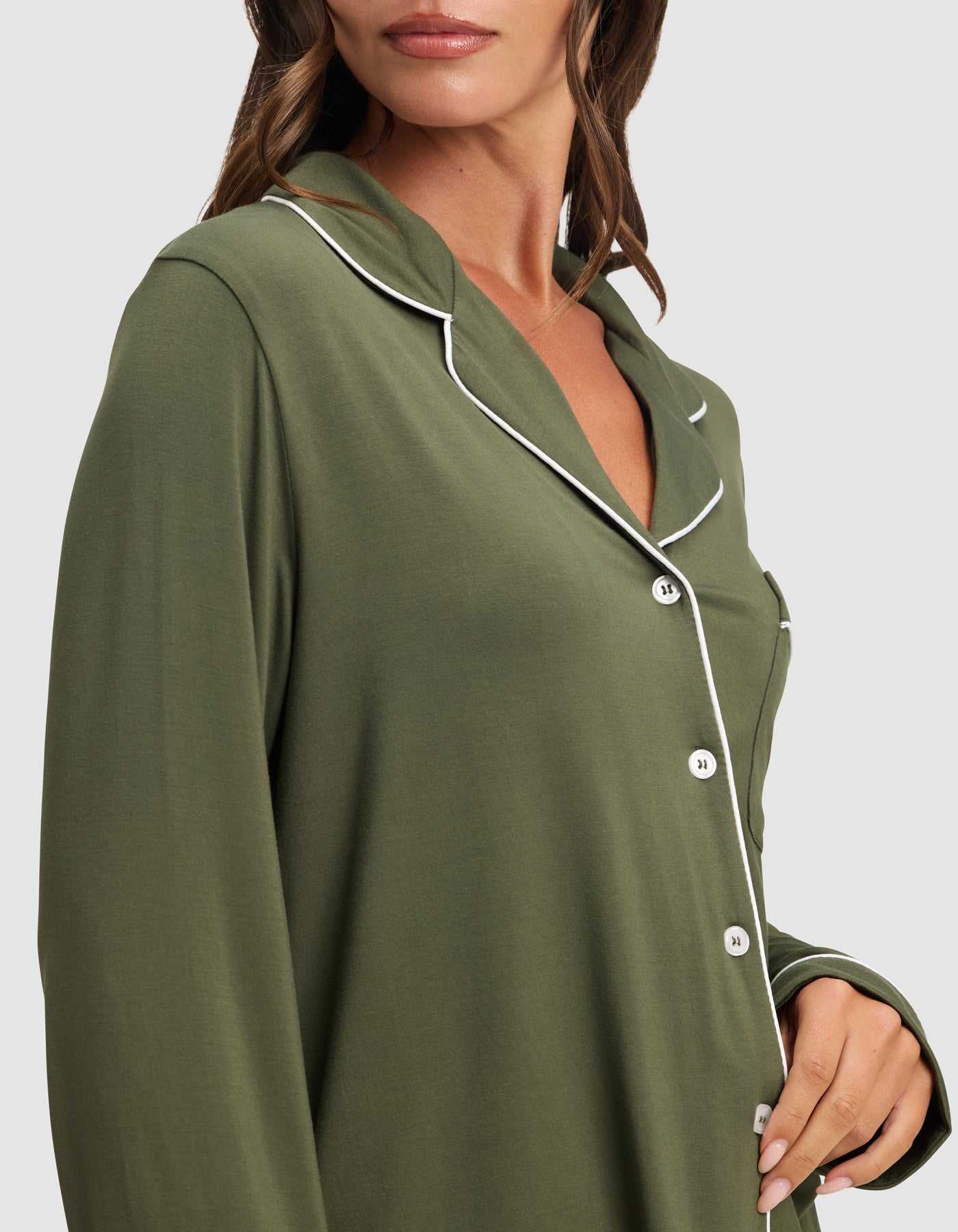 A woman wears the HIDE Women's Bamboo Stretch-Knit Long Sleeve Pajama Top in olive green with white piping and buttons, pictured from shoulders to hips with the collar and part of her face visible. |Color:Olive