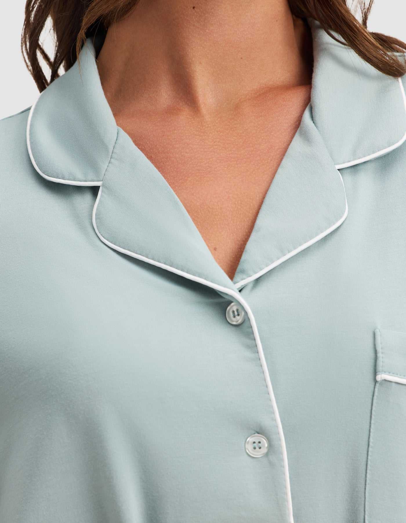 Close-up of a person wearing the Cozy Earth Women's Bamboo Stretch-Knit Long Sleeve Pajama Set in light blue, featuring white piping, a collar, buttons, and a pocket. The image highlights the upper chest, collar, shoulder, and pocket details. |Color:Brook
