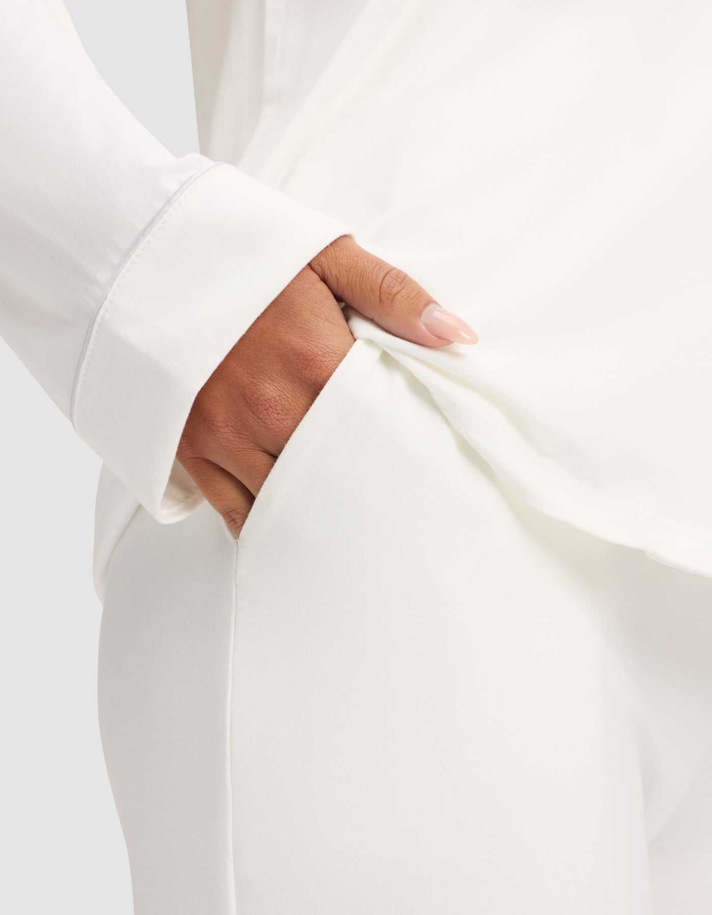A person wears the Cozy Earth Women's Bamboo Stretch-Knit Long Sleeve Pajama Set in white, placing their right hand in the pocket of their white pajama pants. Only their torso, arm, and hand show against a light background. |Color:Ivory