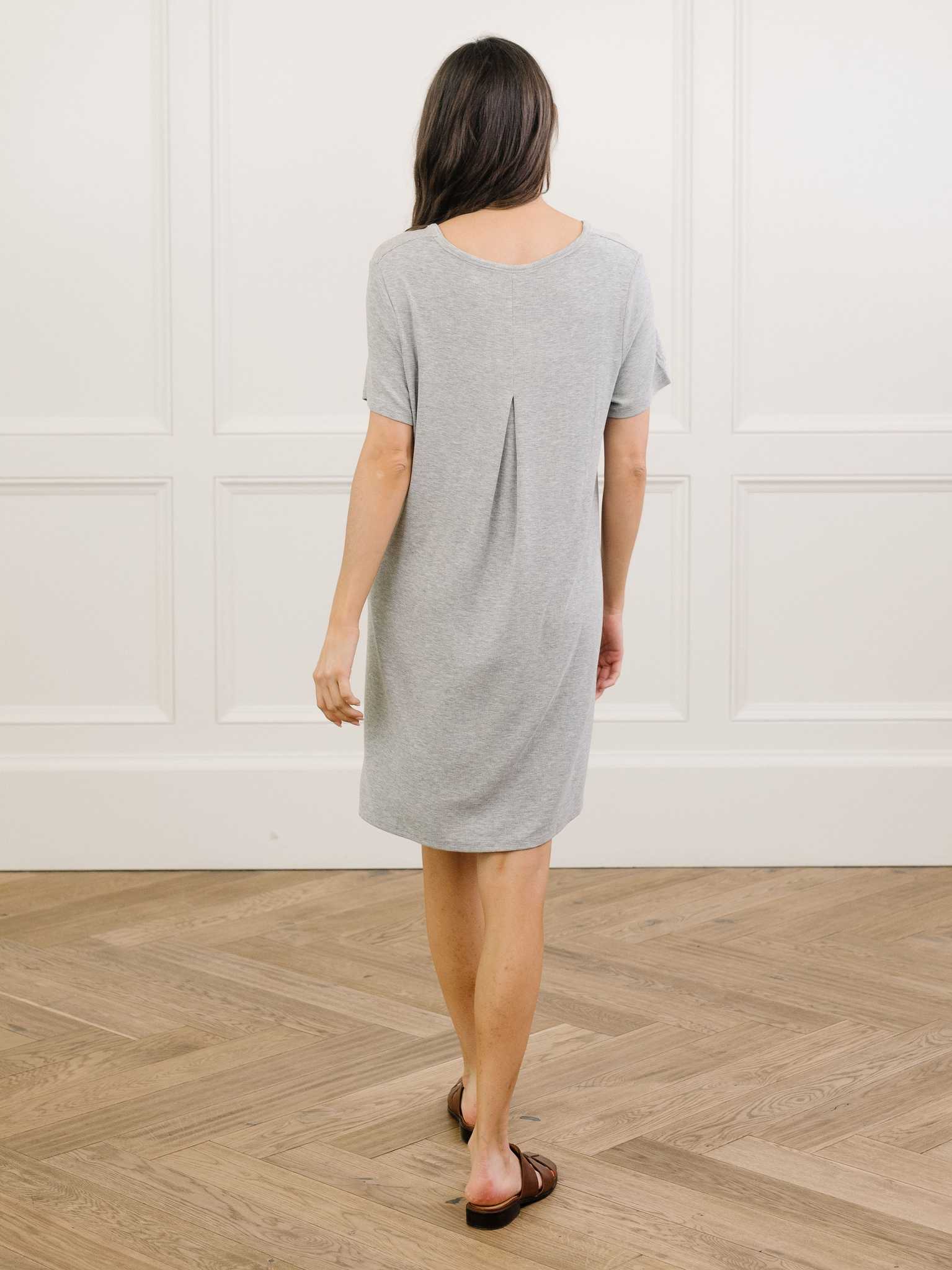 A woman facing backwards standing in a grey Cozy Earth bamboo rib-knit boyfriend sleep dress with short sleeves, knee-length, in a lounge or bedroom setting. |Color:Grey