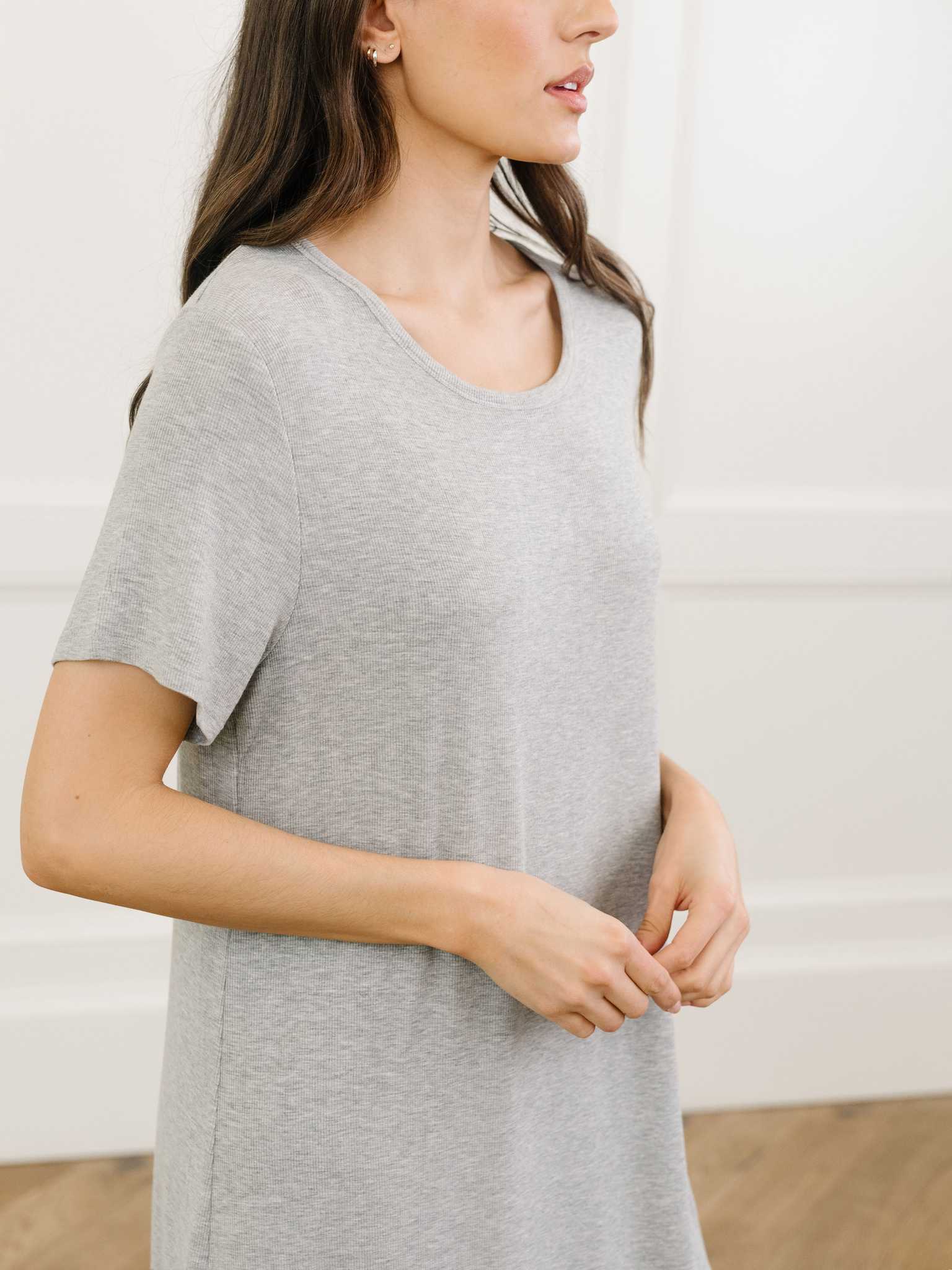 A woman standing in a grey Cozy Earth bamboo rib-knit boyfriend sleep dress with short sleeves, in a lounge or bedroom setting. |Color:Grey