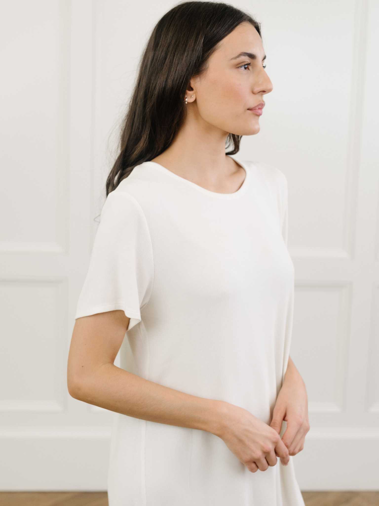 A woman standing in a white Cozy Earth bamboo rib-knit boyfriend sleep dress with short sleeves, knee-length, in a lounge or bedroom setting. |Color:Ivory
