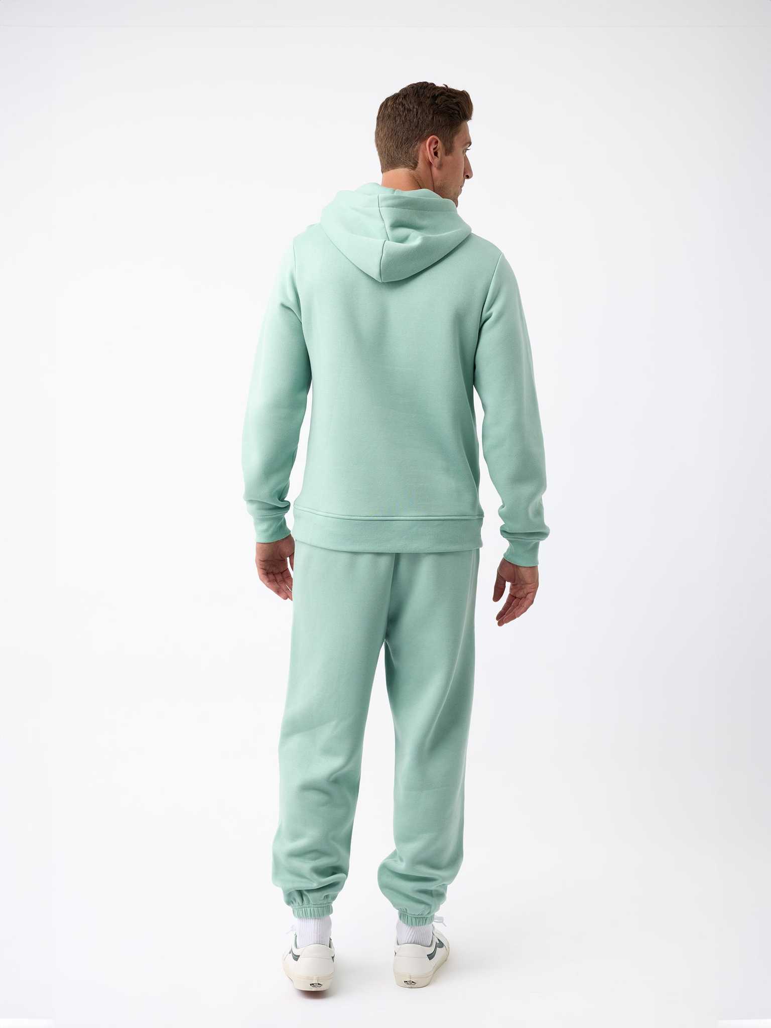 A person wearing a Men's CityScape Hoodie in light green from Cozy Earth, with matching sweatpants, stands facing away from the camera on a plain white background and is sporting white sneakers. |Color:Wintergreen