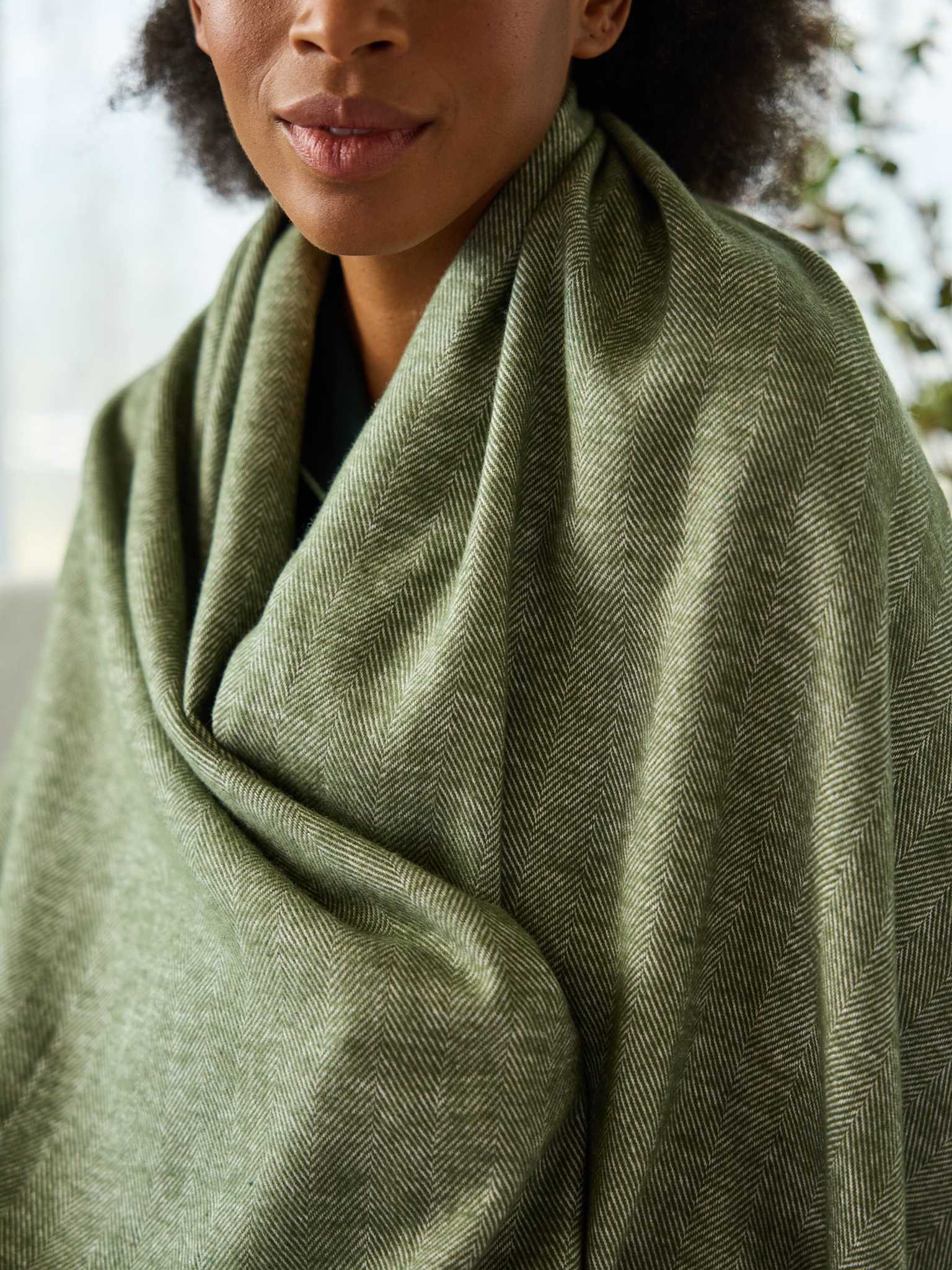 Close up of woman with ivy herringbone tassel throw wrapped around her |Color:Ivy