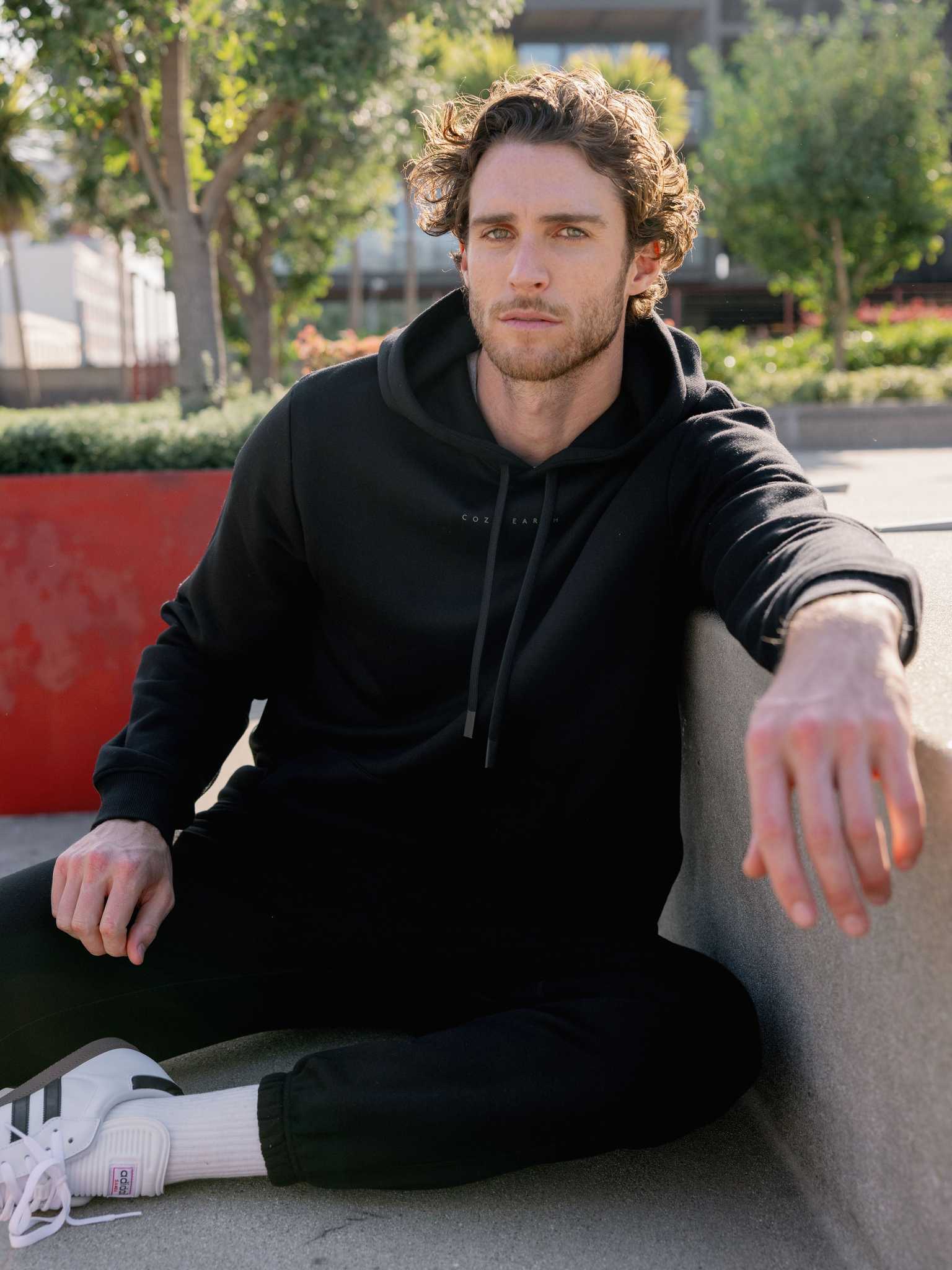 Man sitting on city bench wearing black cityscape hoodie and sweats |Color:Black