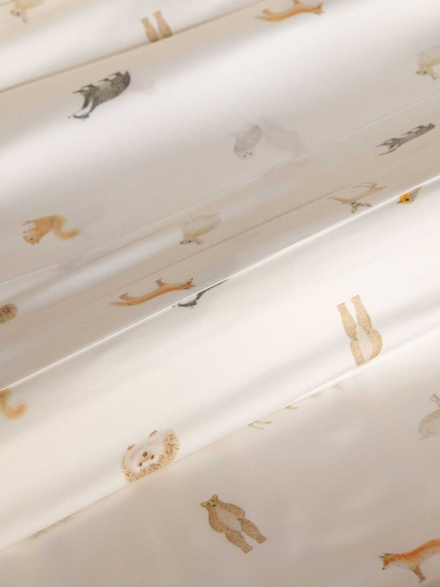 The Bamboo Fitted Sheet by Cozy Earth features a white fabric adorned with small, subtle illustrations of various animals like bears, foxes, and rabbits, evenly spaced across the surface. |Color:Woodland Creatures