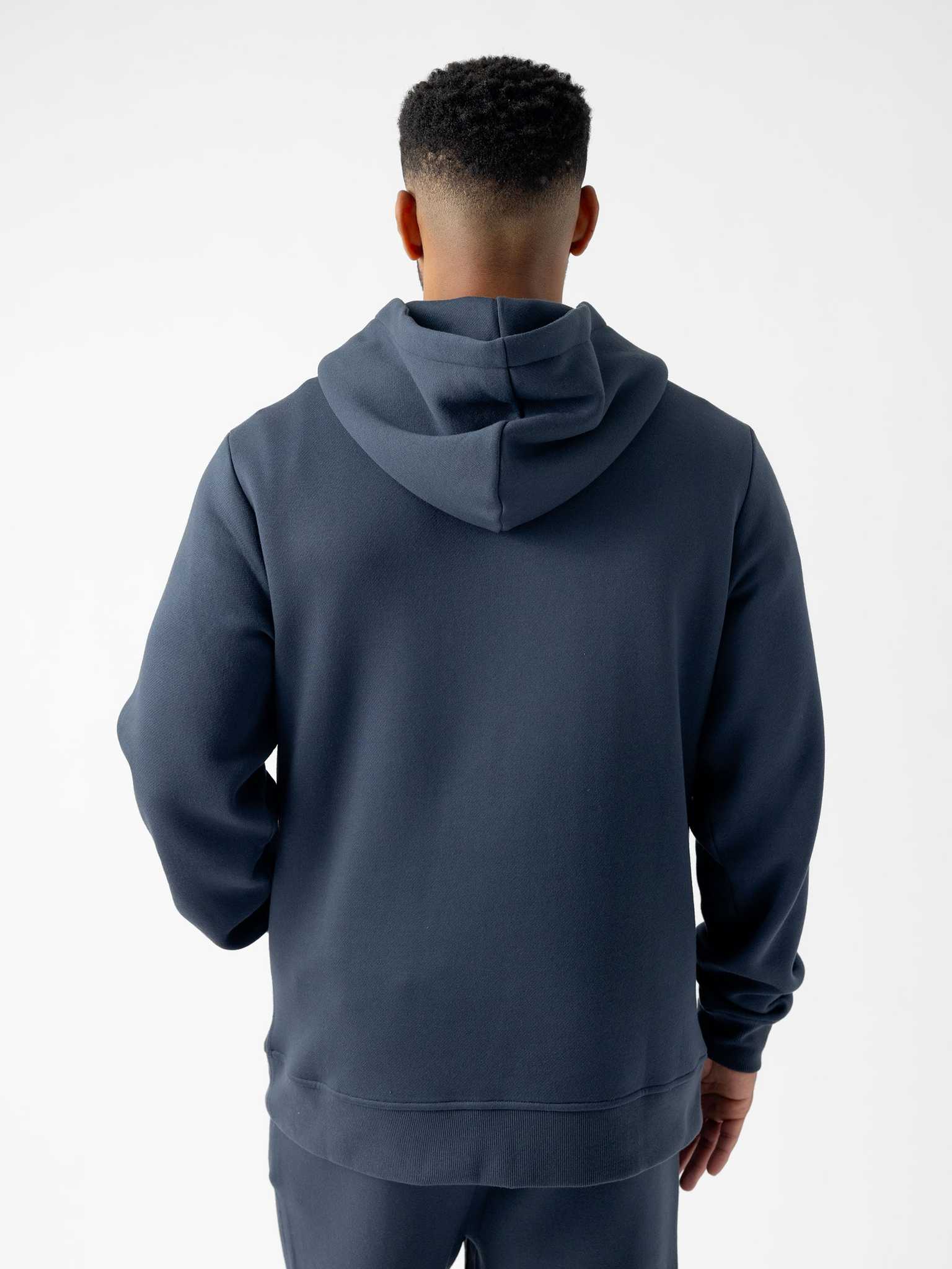 A person with short hair is seen from behind wearing a dark, long-sleeved Men's CityScape Hoodie by Cozy Earth. The background is plain and white. |Color:Eclipse