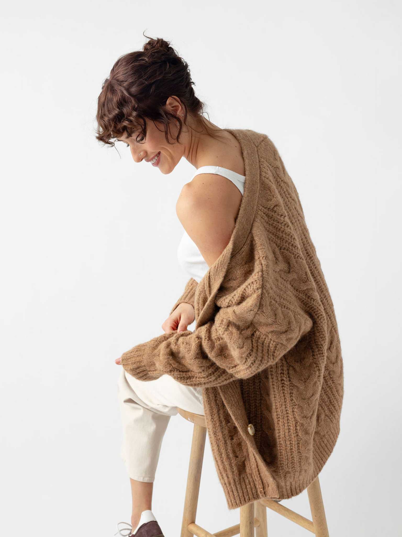 Woman sitting on wooden stool wearing camel cardigan off the shoulder |Color:Camel