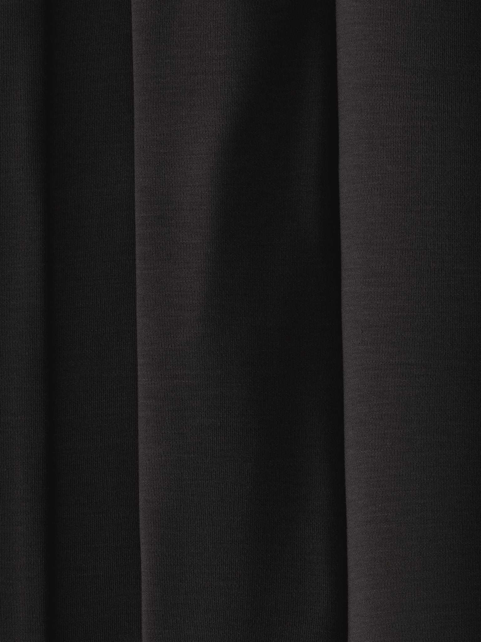 A close-up of dark, evenly folded fabric from the Women's Bedtime Bundle by Cozy Earth, with deep shadows and a smooth texture. The image shows parallel vertical lines formed by the folds, creating an elegant and understated appearance. |Color:Black