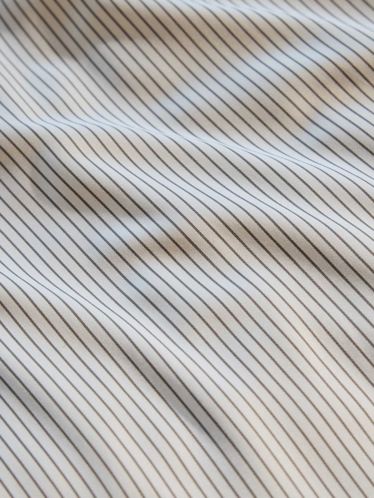 Close-up of the Bamboo Duvet Cover by Cozy Earth, showcasing a textured design with thin, parallel black and white stripes. The duvet cover surface appears to have gentle waves, creating subtle shadows and highlights. |Color:Charcoal Pinstripe