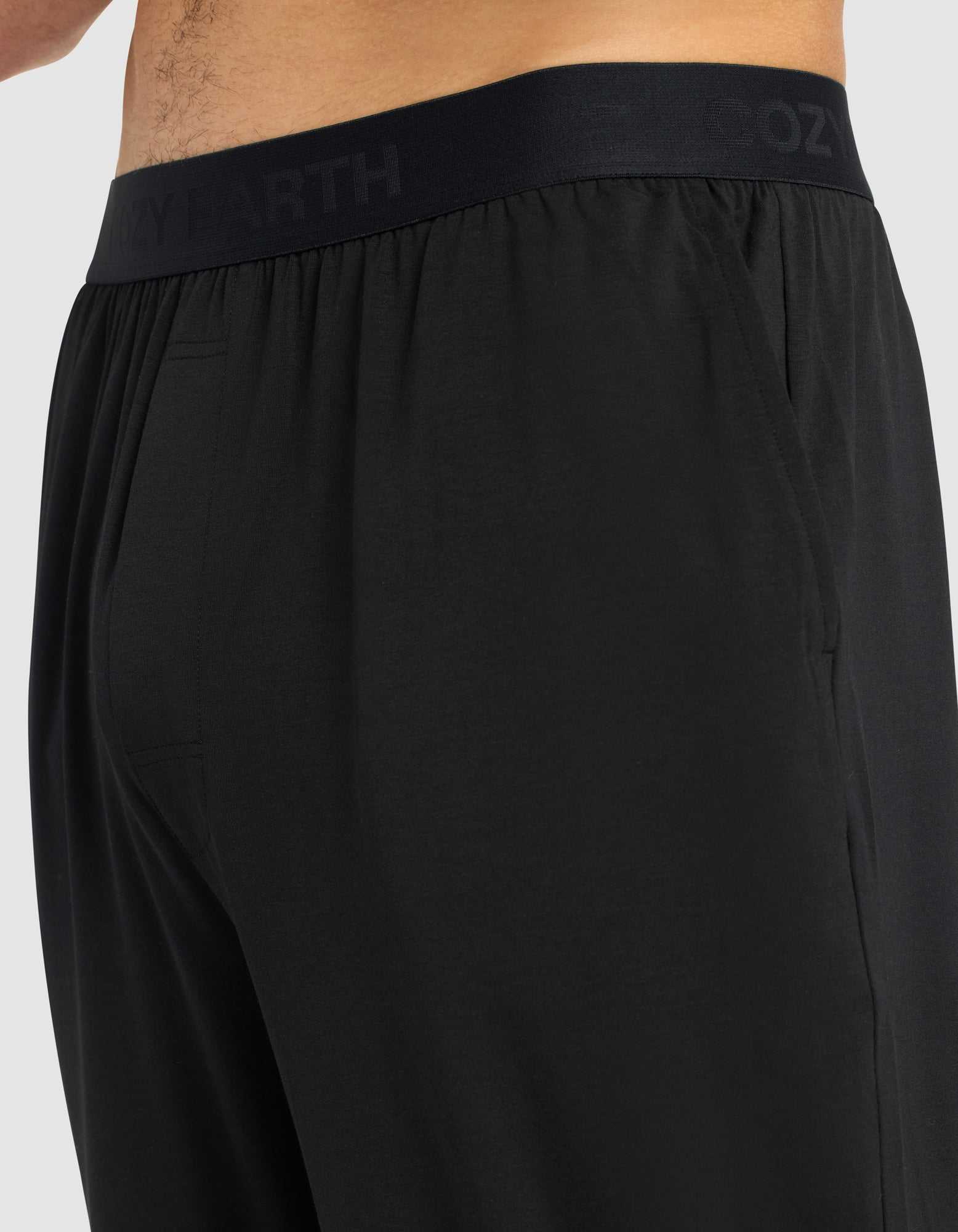 Close-up side view of a person wearing Cozy Earth Men's First Layer Pajama Pant, featuring an elastic waistband subtly printed with "COZY EARTH." The soft, smooth fabric enhances comfort.|Color:Jet Black