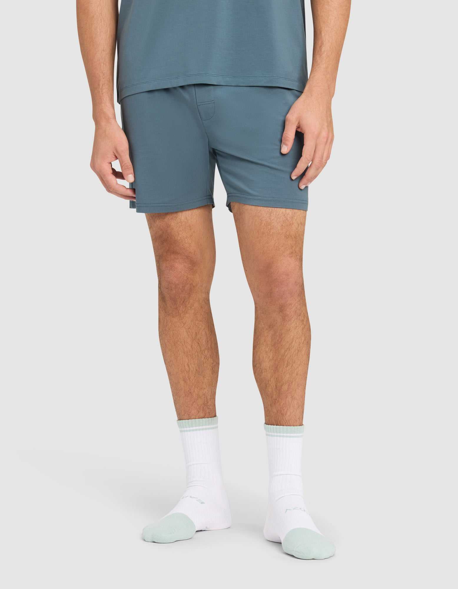 A person stands against a plain background wearing Cozy Earth's Men's First Layer Pajama Short and matching shirt, paired with white socks featuring mint green toes and heels. The image is cropped at the mid-torso. |Color:Dawn