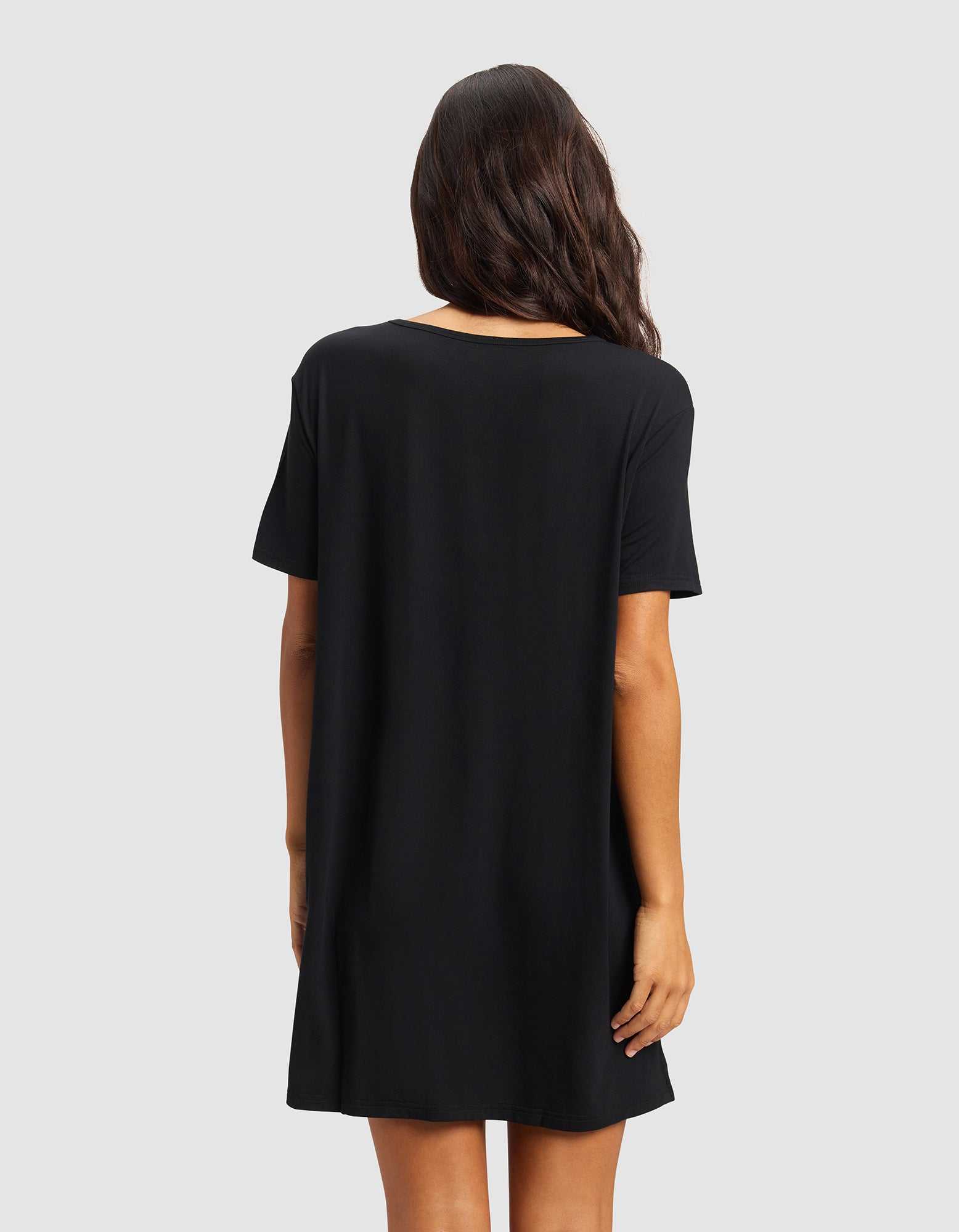 A woman with long, wavy dark hair is shown from the back, wearing the Cozy Earth Women's Bamboo Stretch-Knit Sleep Dress in black against a plain light gray background.|Color:Black