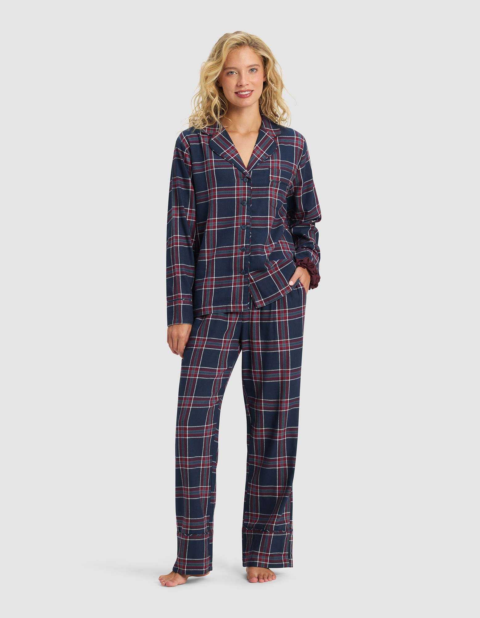 A woman stands barefoot, smiling in Cozy Earth's Women's Farmhouse Pajama Pant, featuring a navy blue base with red and white plaid. She pairs it with a matching long-sleeve button-up top, posing against a plain light background.|Color:Eclipse Plaid