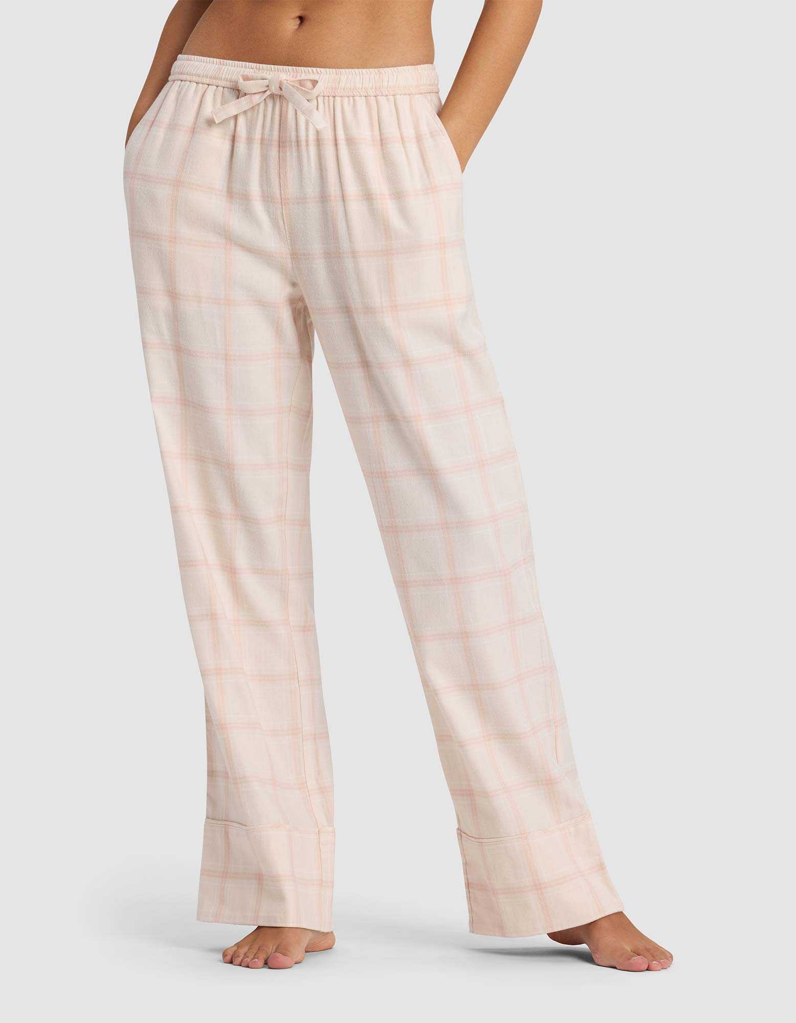 A woman models the Cozy Earth Women's Farmhouse Pajama Pant in light pink plaid, featuring a drawstring waist, while standing barefoot against a plain light background.|Color:Quartz Plaid