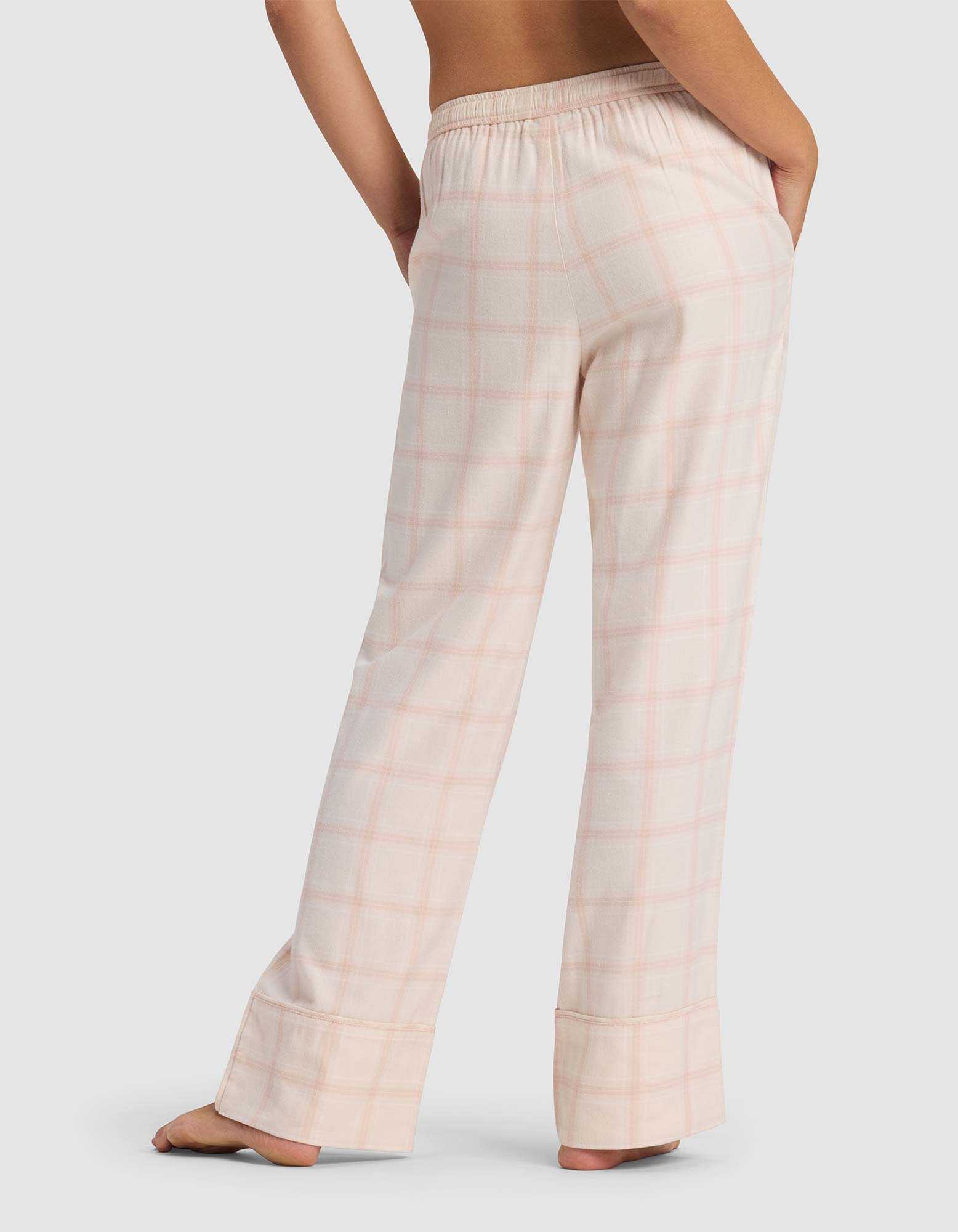 A woman is seen from behind wearing Cozy Earth's Women's Farmhouse Pajama Pant in light pink plaid with an elastic waistband, standing barefoot against a light background.|Color:Quartz Plaid