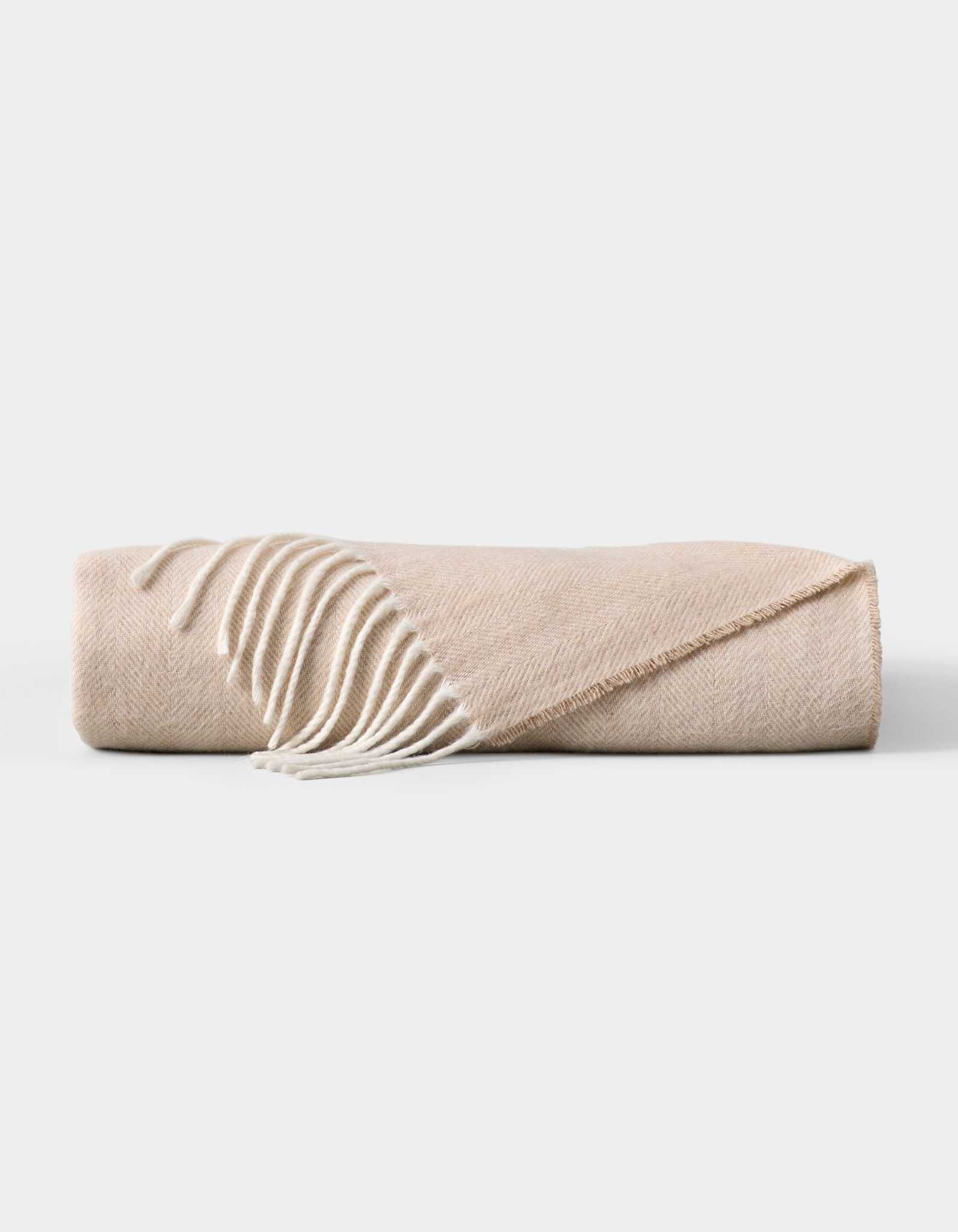 The Cozy Earth Bamboo Herringbone Tassel Throw is a folded beige blanket featuring a subtle herringbone pattern and white tassel fringe on one edge, displayed against a plain white background. |Color:Oatmeal