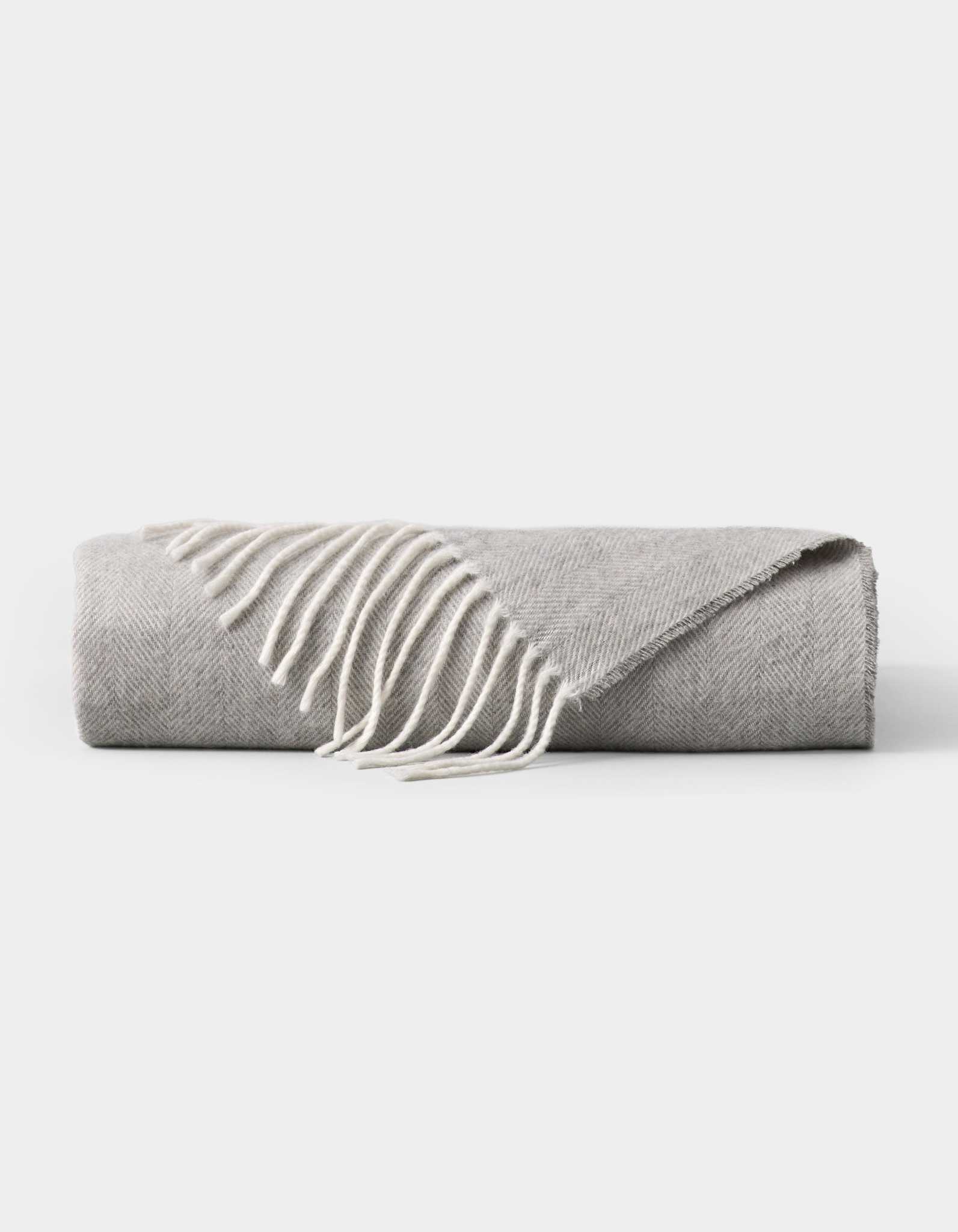 The Bamboo Herringbone Tassel Throw by Cozy Earth, featuring a light gray hue and white fringed edges, is neatly folded and displayed on a plain white background.|Color:Cloud