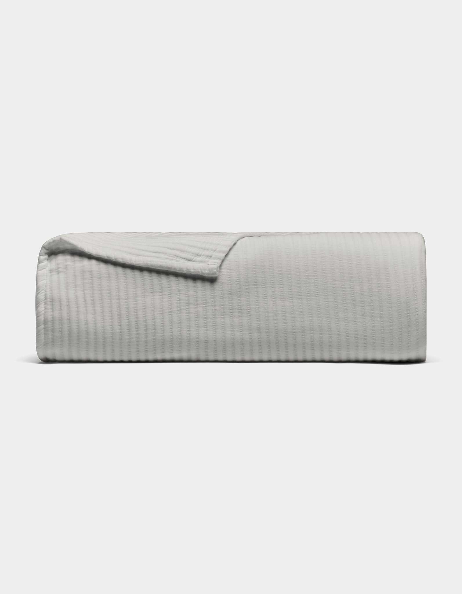The Cozy Earth Bamboo Coverlet, shown in light gray with a textured design, is neatly folded against a plain white background. A corner is turned down to display its soft material.|Color:Light Grey