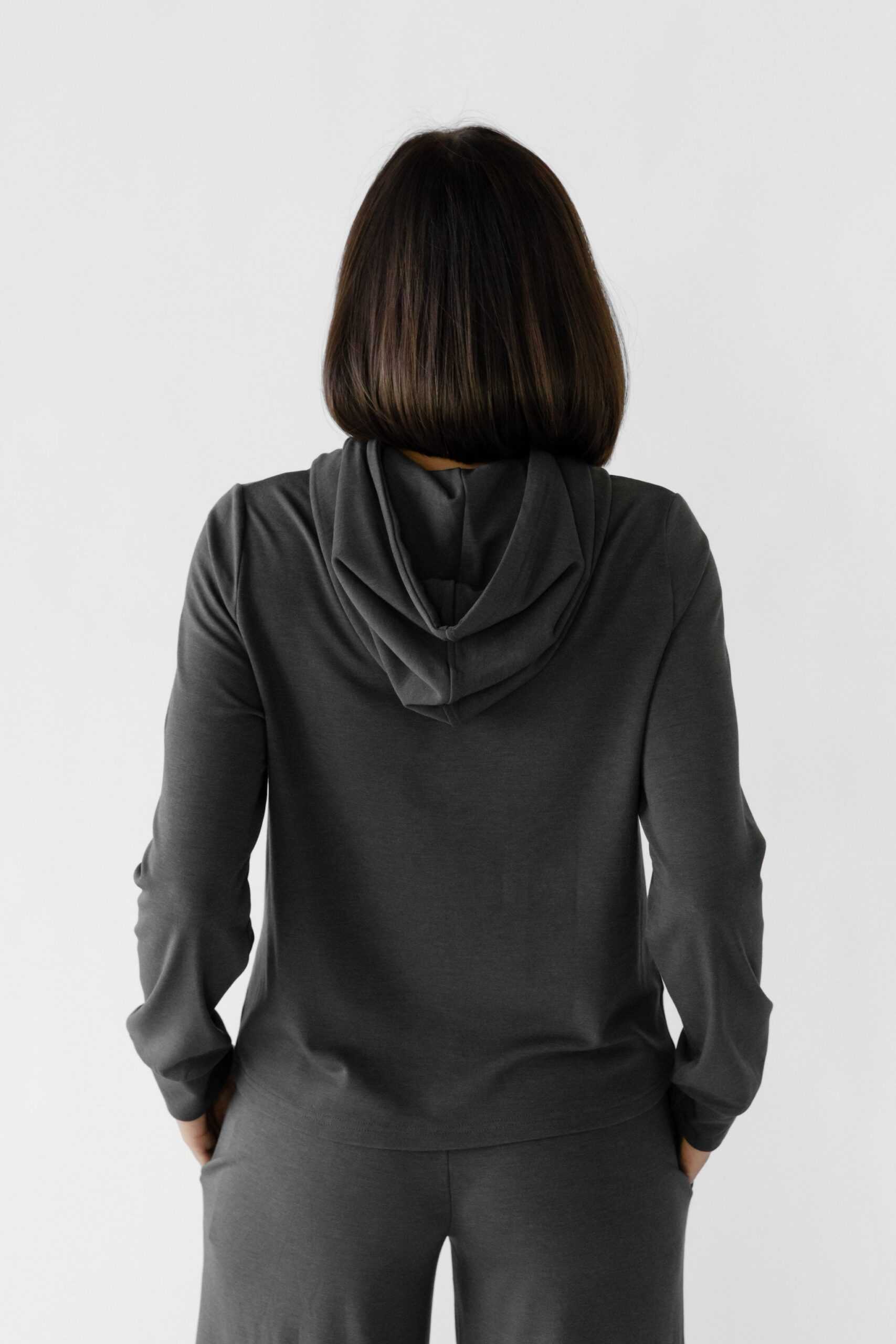 A woman wearing a grey Cozy Earth Brushed Bamboo Hoodie with a drawstring and sleeve cuffs. The hoodie has an embroidered logo on the front. |Color:Charcoal