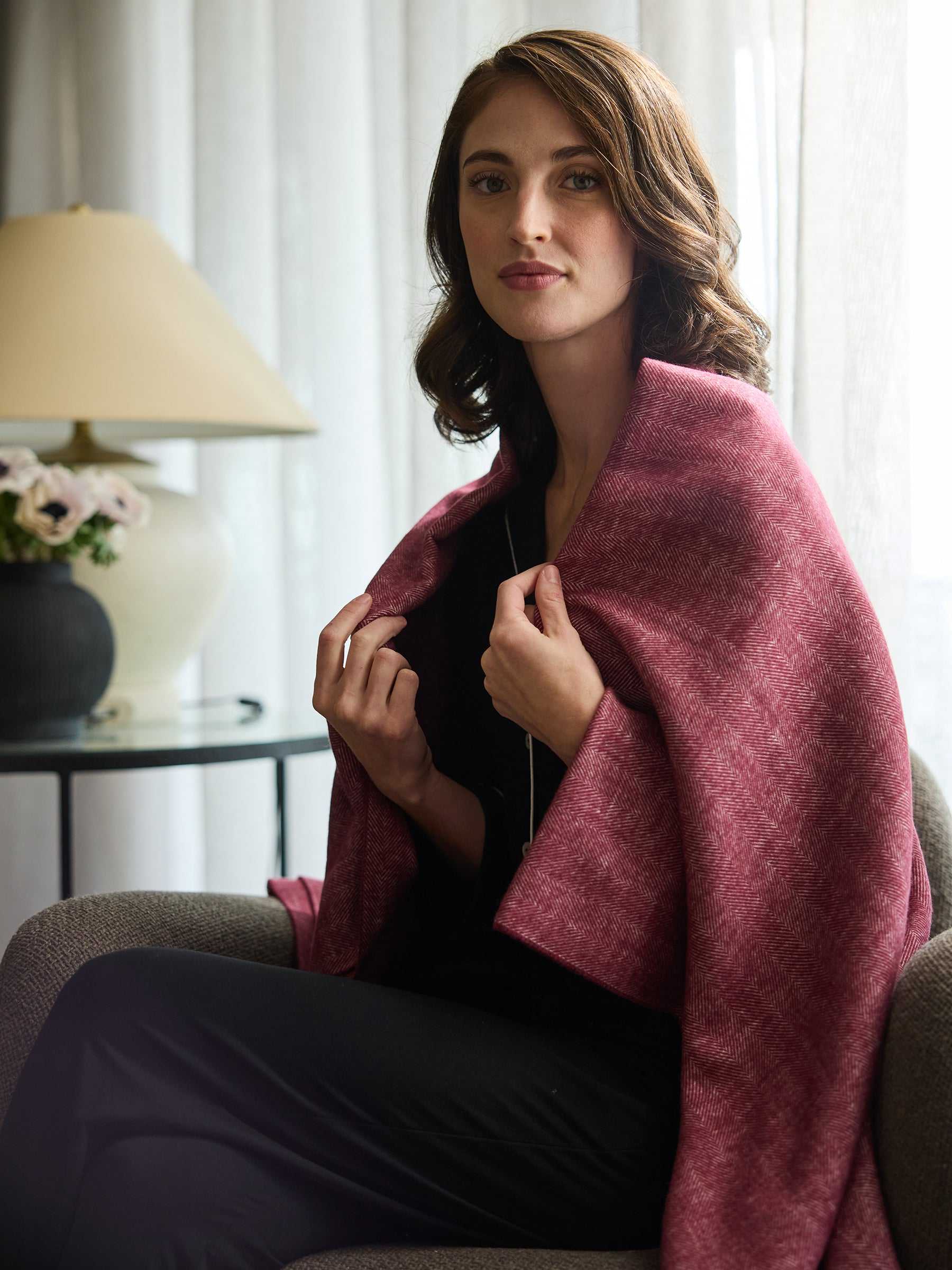 Woman sitting down with berry herringbone tassel throw wrapped around her |Color:Berry
