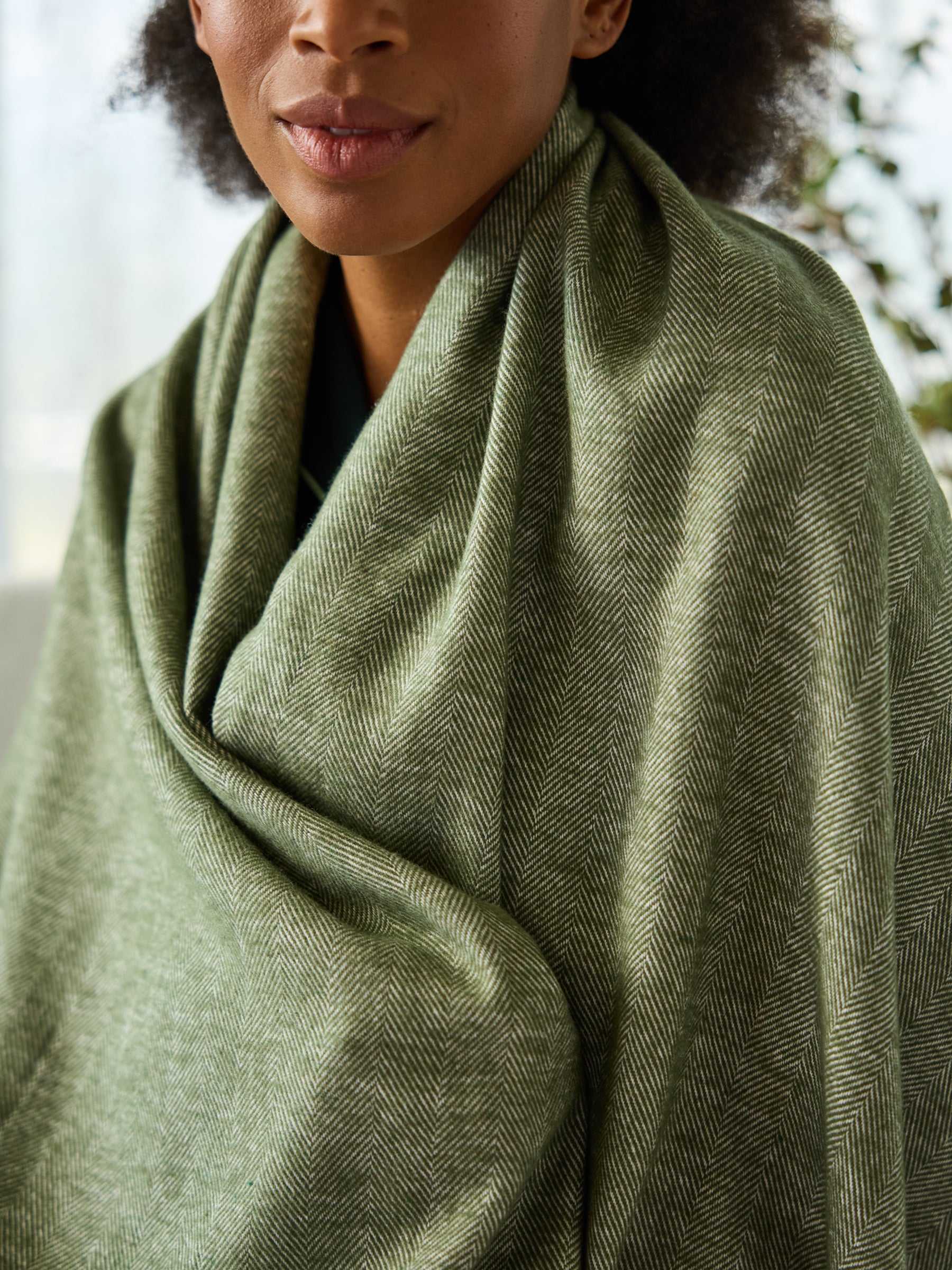 Close up of woman with ivy herringbone tassel throw wrapped around her |Color:Ivy