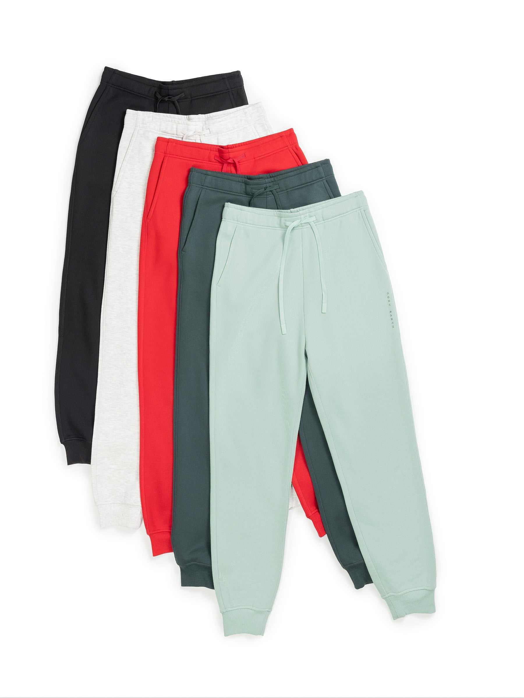 Five pairs of Men's CityScape Joggers by Cozy Earth in a variety of colors—black, white, red, dark green, and light green—are displayed overlapping each other with drawstrings visible. The joggers feature elastic cuffs at the ankles. |Color:Black