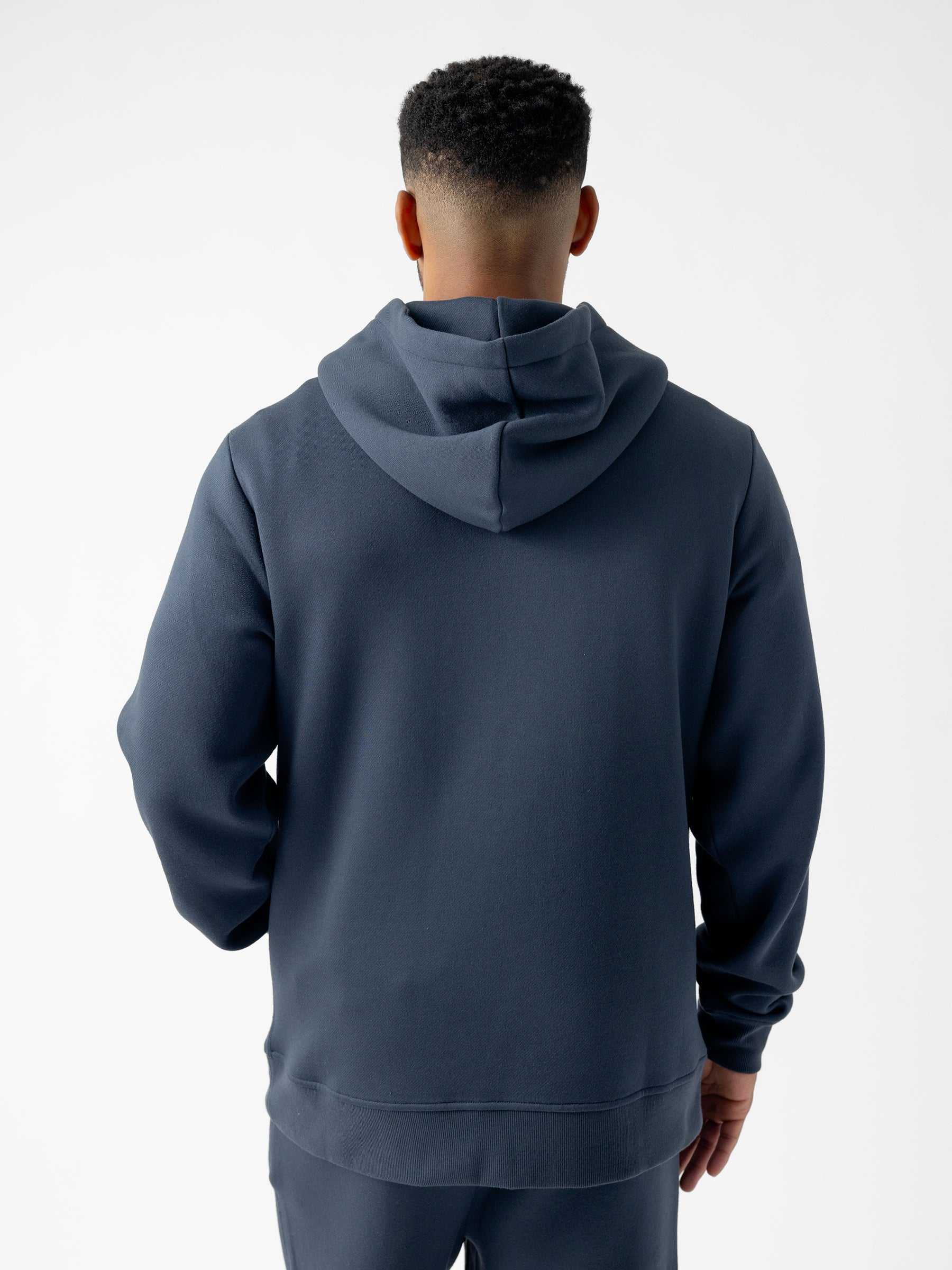 A person with short hair is seen from behind wearing a dark, long-sleeved Men's CityScape Hoodie by Cozy Earth. The background is plain and white. |Color:Eclipse