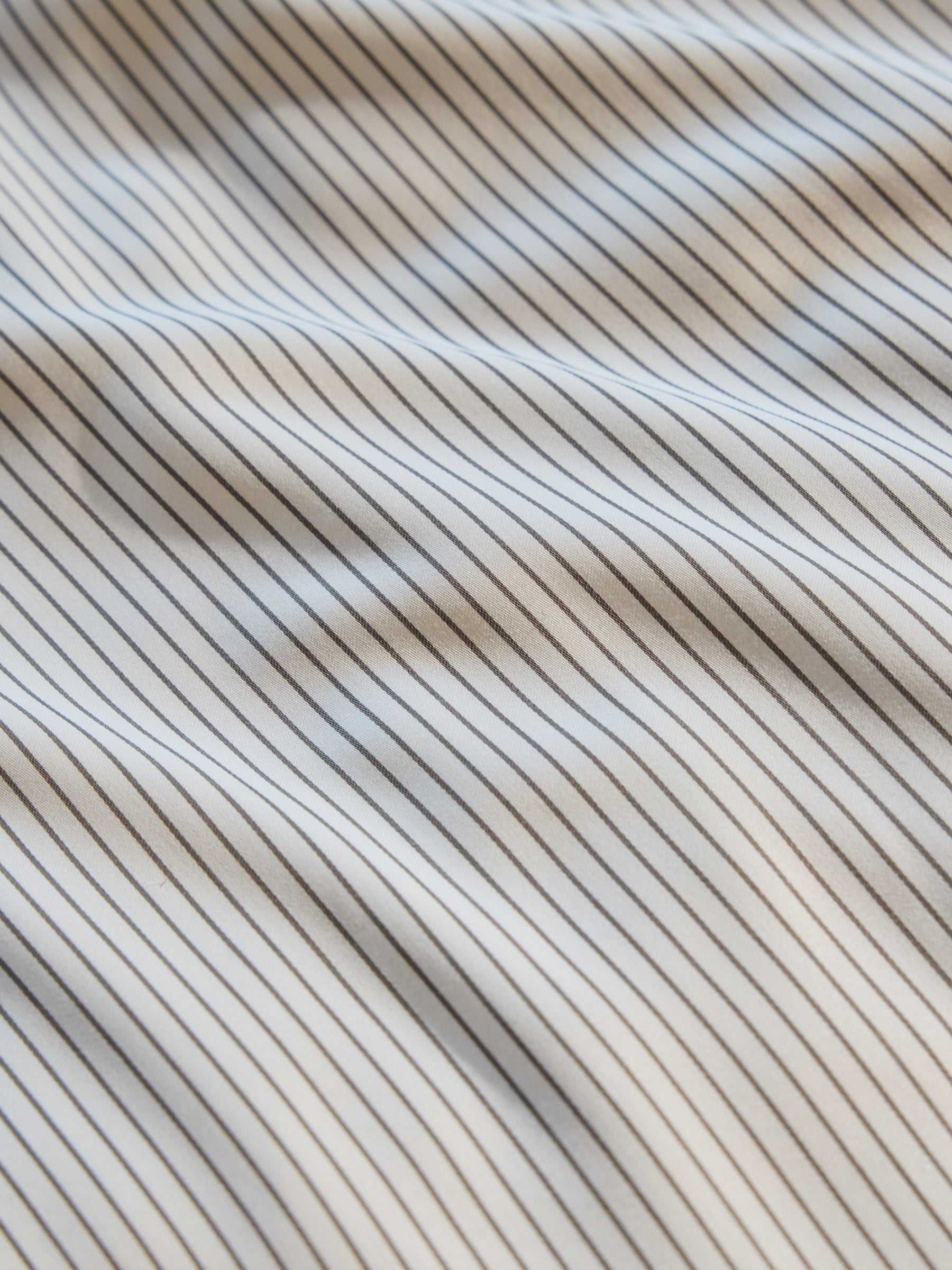 Close-up of the Bamboo Duvet Cover by Cozy Earth, showcasing a textured design with thin, parallel black and white stripes. The duvet cover surface appears to have gentle waves, creating subtle shadows and highlights. |Color:Charcoal Pinstripe