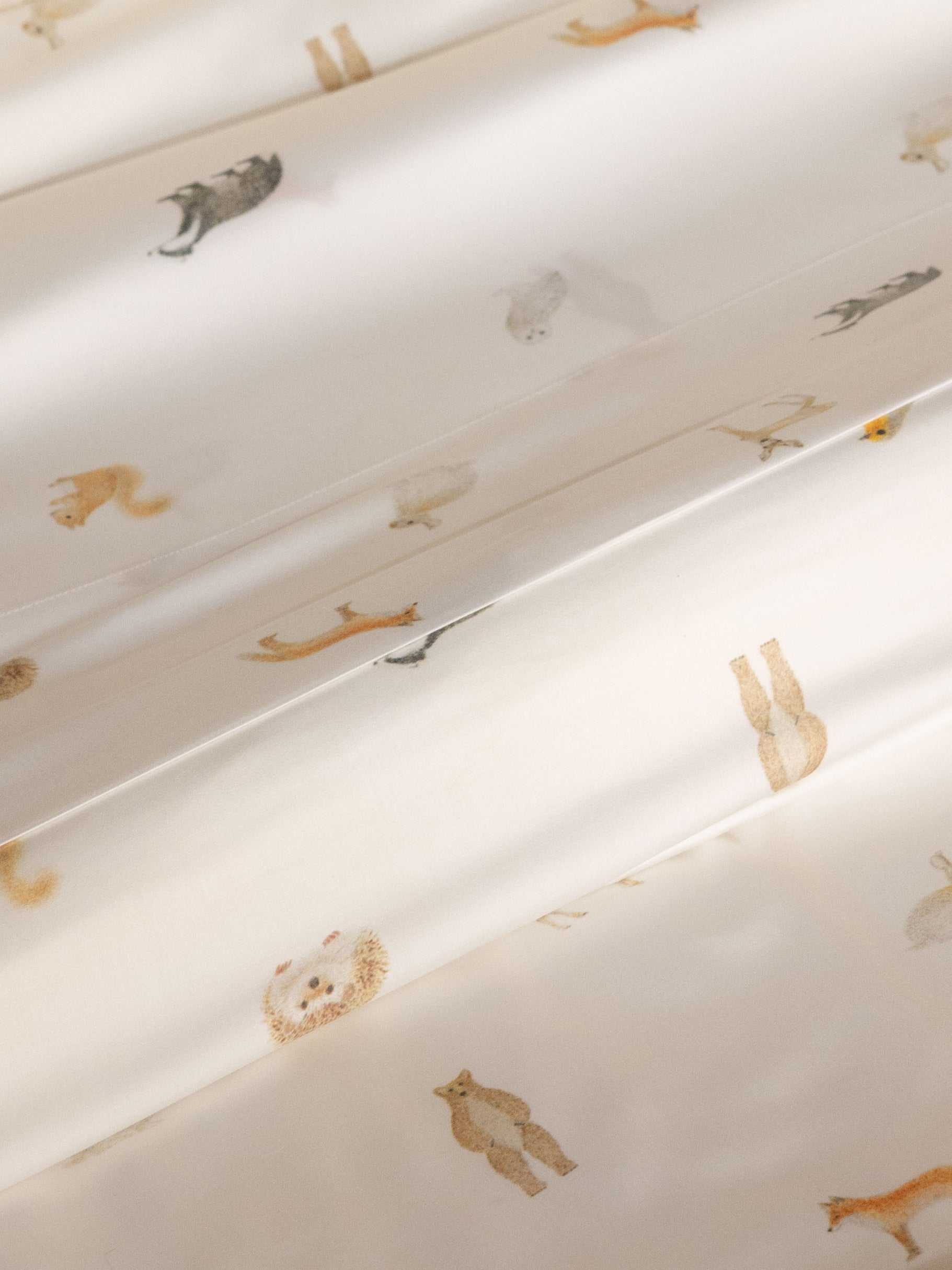 The Bamboo Fitted Sheet by Cozy Earth features a white fabric adorned with small, subtle illustrations of various animals like bears, foxes, and rabbits, evenly spaced across the surface. |Color:Woodland Creatures
