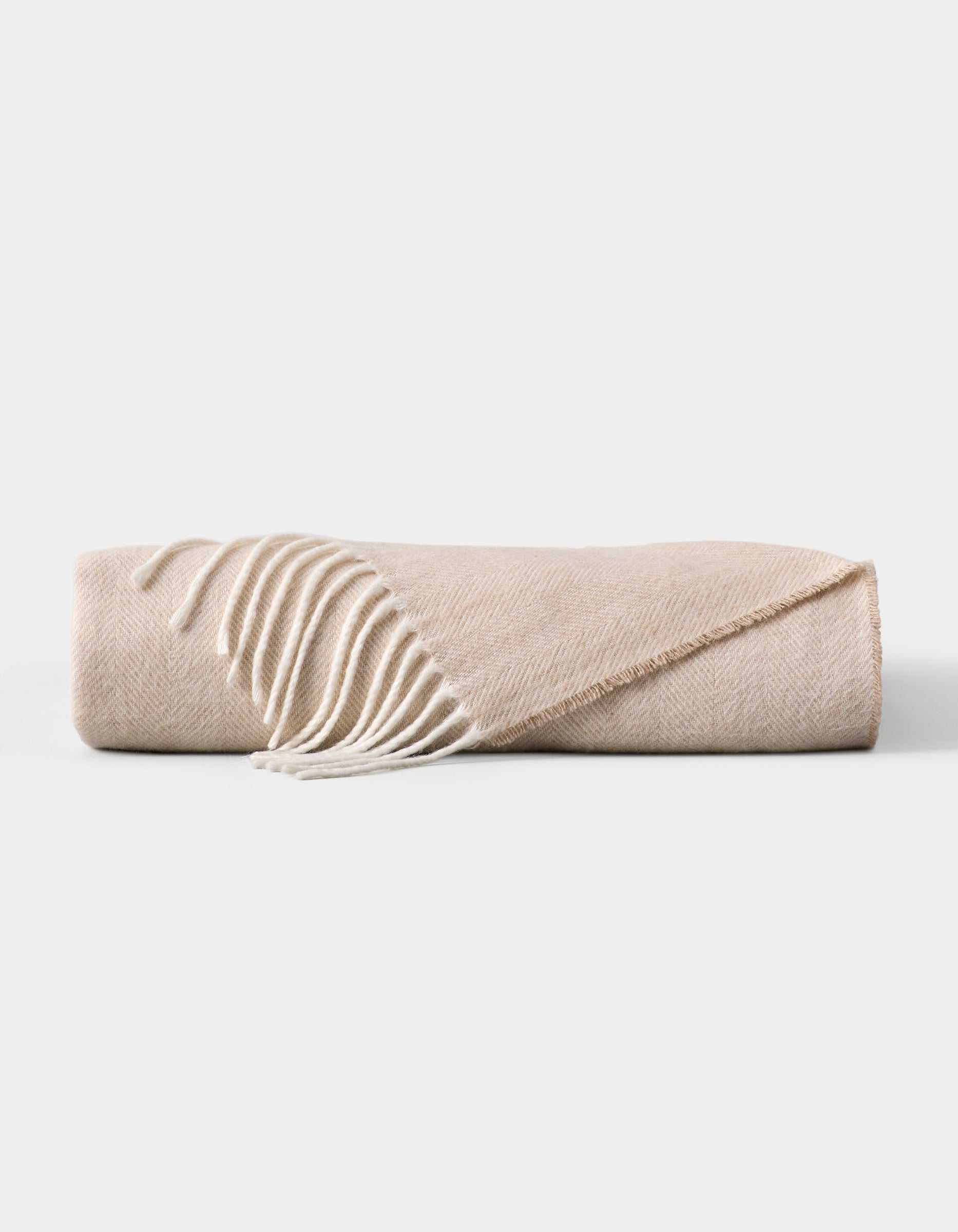 The Cozy Earth Bamboo Herringbone Tassel Throw is a folded beige blanket featuring a subtle herringbone pattern and white tassel fringe on one edge, displayed against a plain white background. |Color:Oatmeal