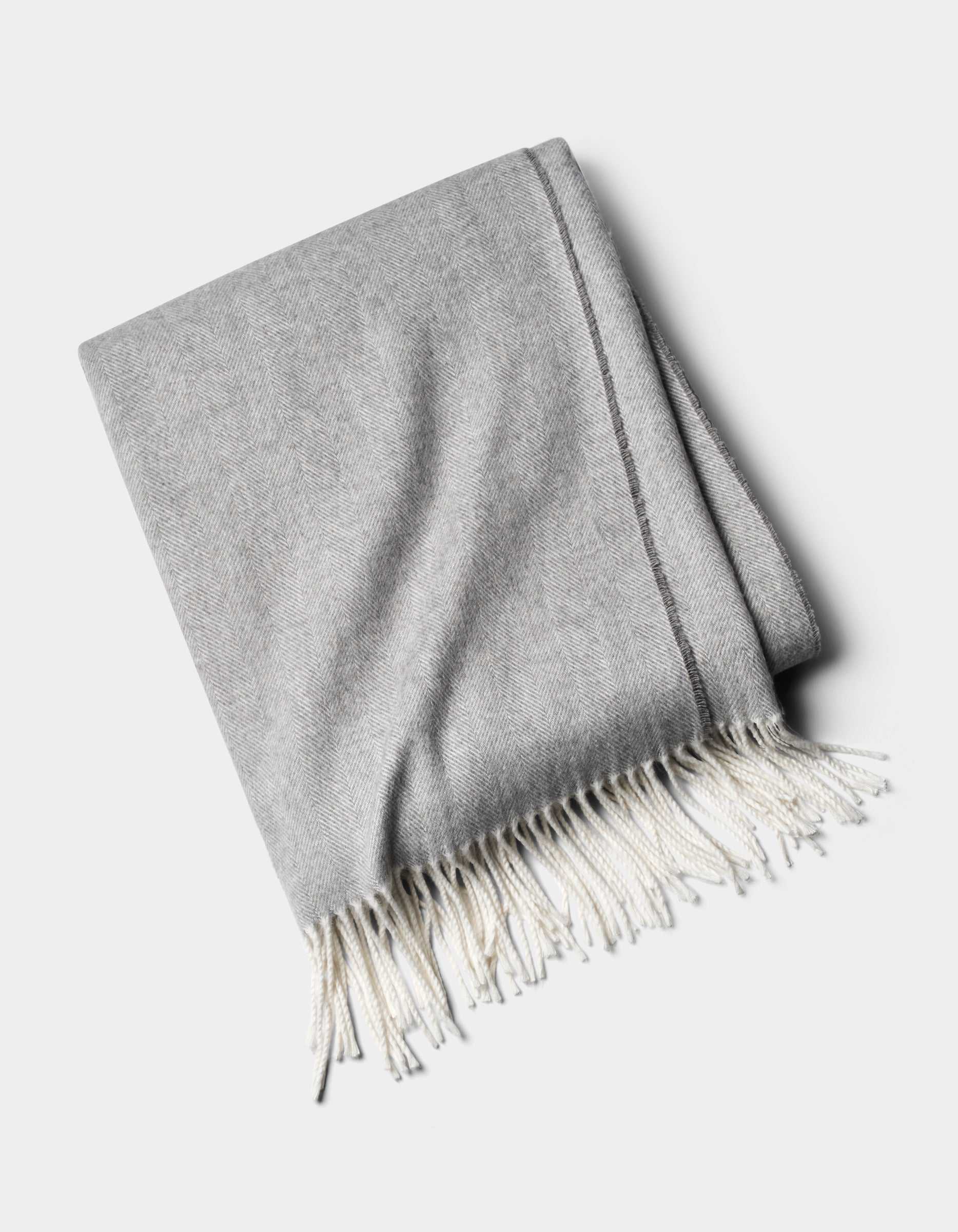The Cozy Earth Bamboo Herringbone Tassel Throw is a folded light gray blanket with white fringed tassels on one edge, shown against a plain white background.|Color:Cloud