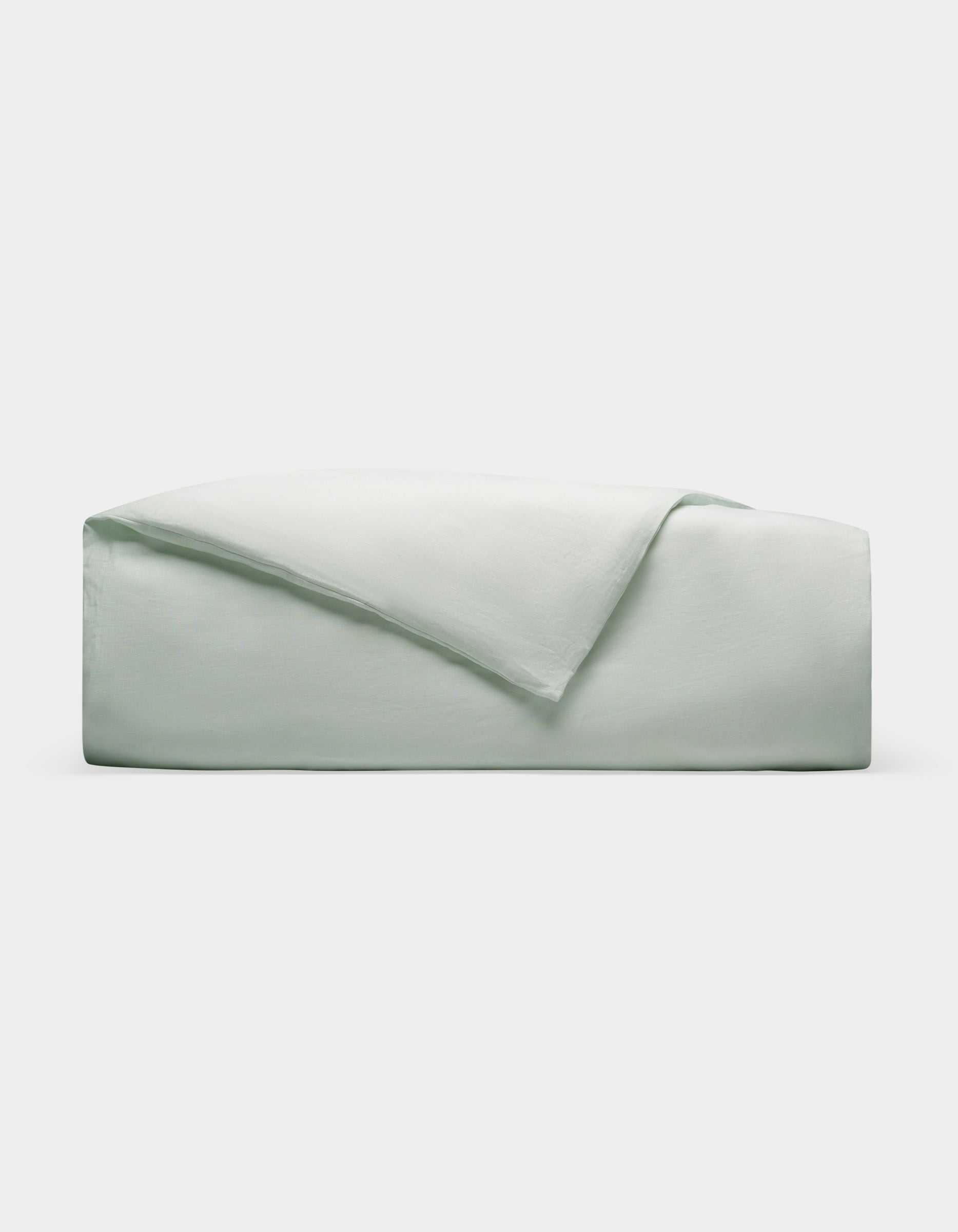 A Cozy Earth Linen Duvet Cover, neatly folded in light gray or pale green, is stacked on a plain white background.|Color:Mist