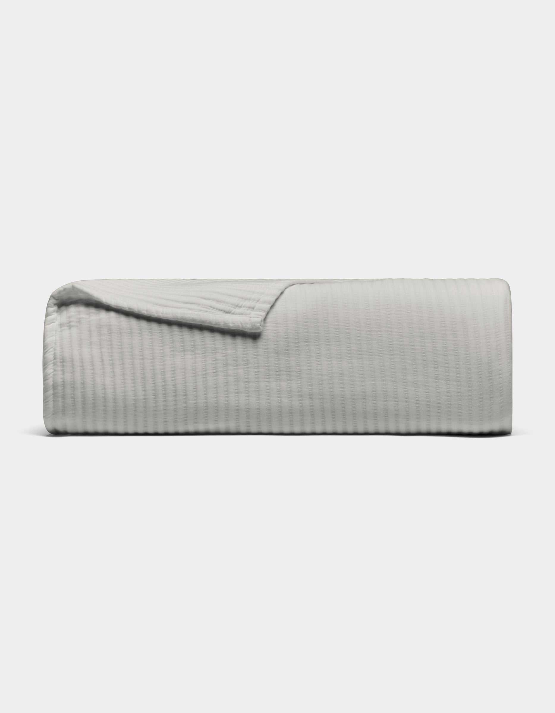 The Cozy Earth Bamboo Coverlet, shown in light gray with a textured design, is neatly folded against a plain white background. A corner is turned down to display its soft material.|Color:Light Grey