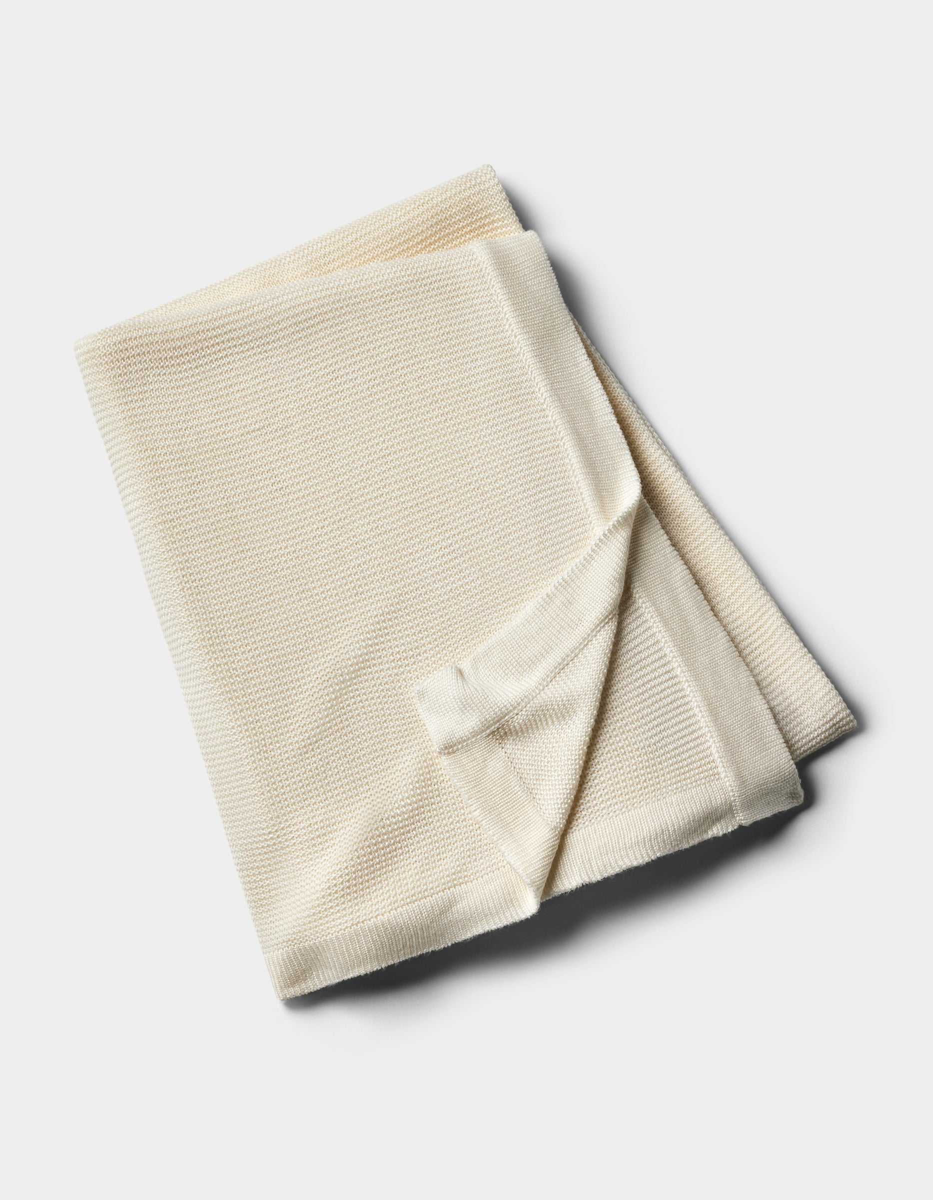 The Cozy Earth Cloud Knit Blanket by Cozy Earth, in a cream hue, is neatly folded and displayed on a plain white background.|Color:Ivory