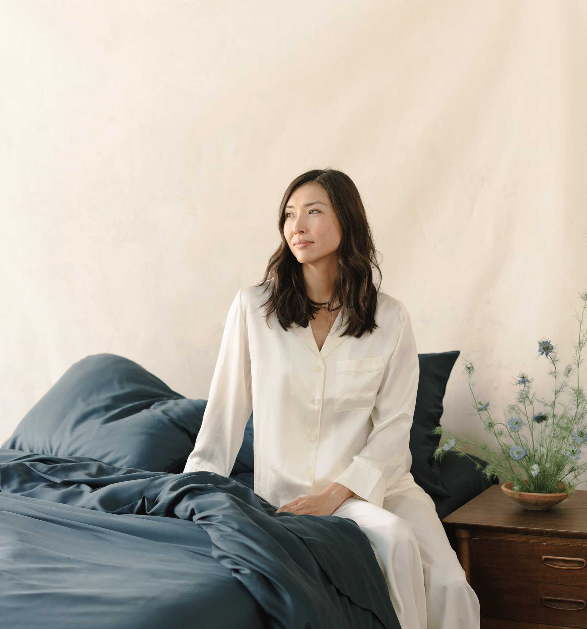 Woman in white pajamas sitting on bed with navy bedding |Color:Navy
