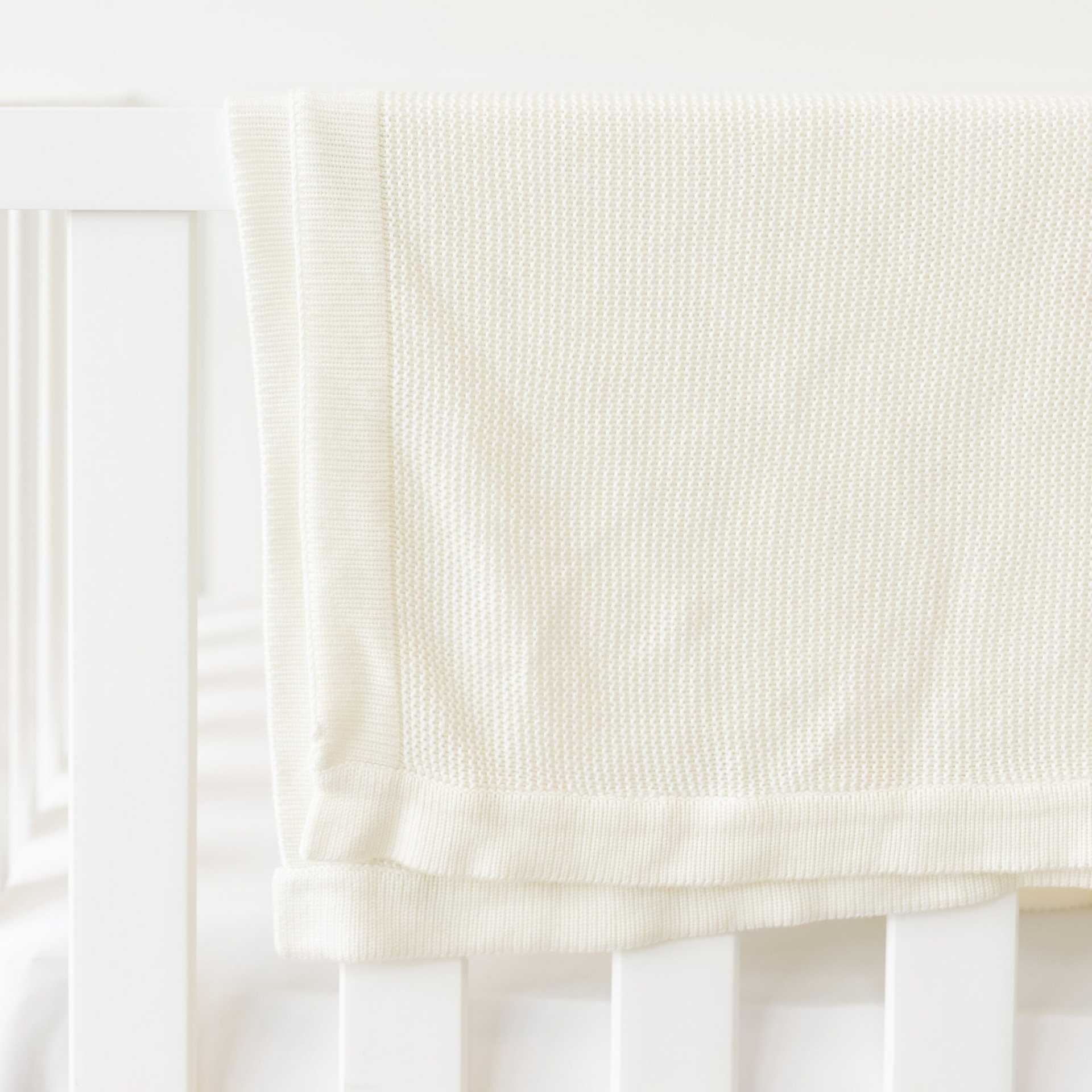 Ivory Cloud Knit Baby Blanket draped over crib |Color:Ivory