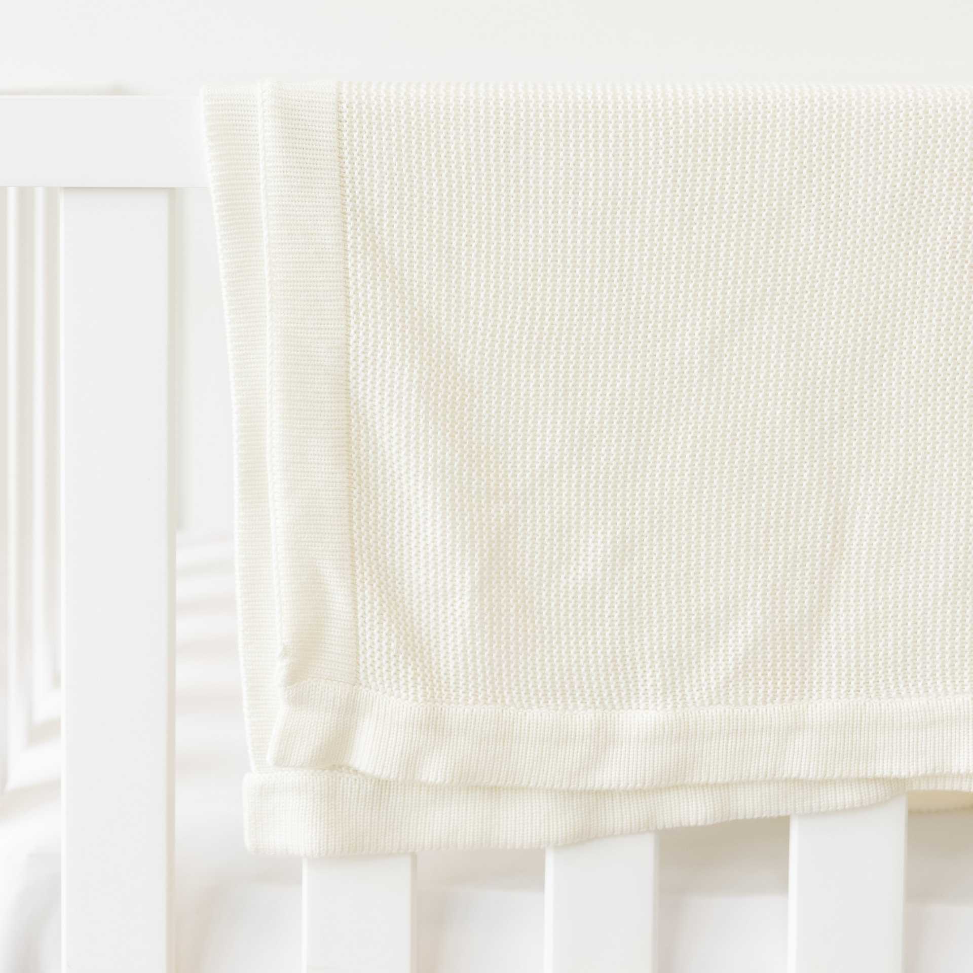 Ivory Cloud Knit Baby Blanket draped over crib |Color:Ivory