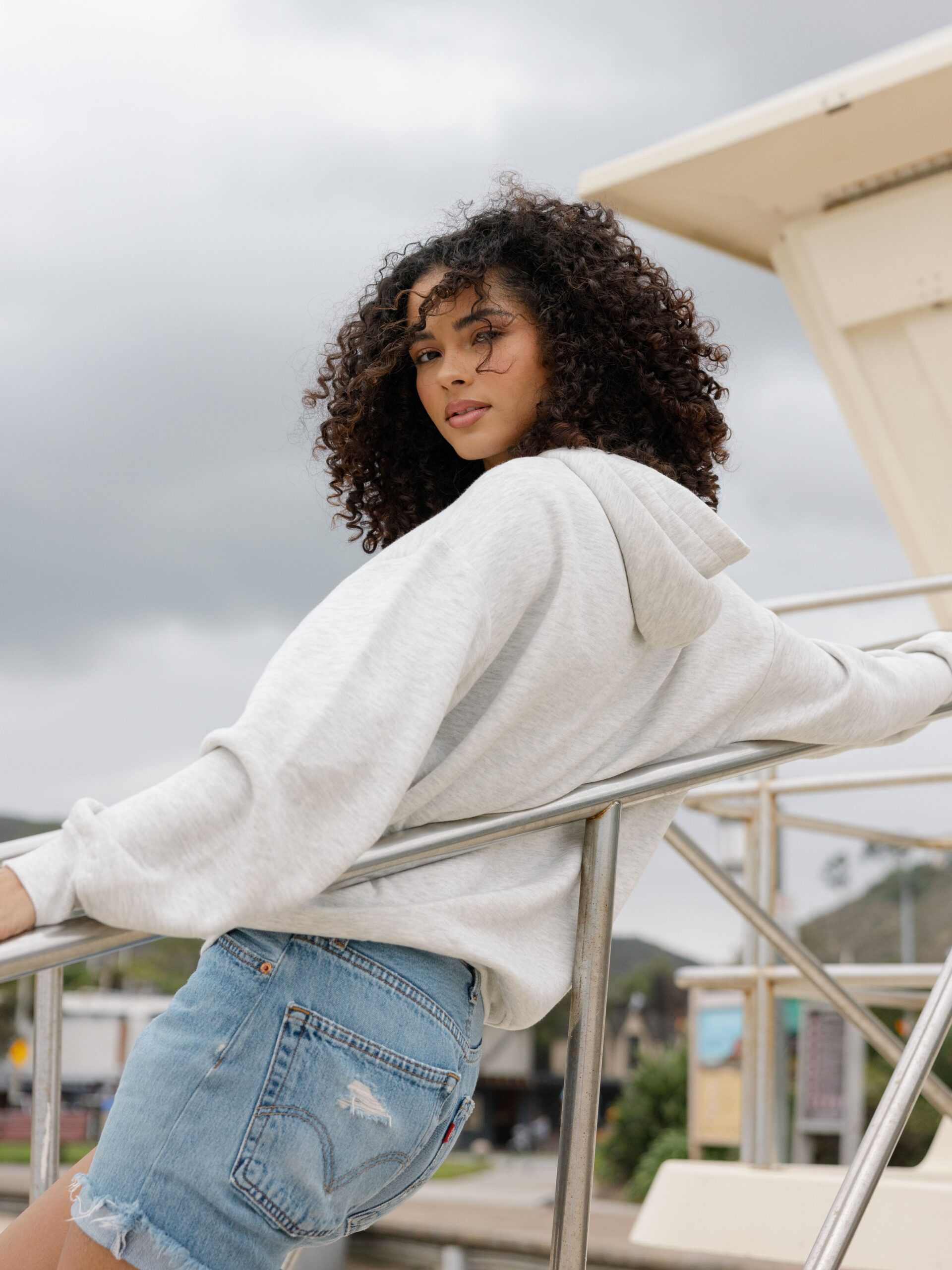 Back of woman wearing jorts and heather grey cityscape hoodie on the beach |Color:Heather Grey