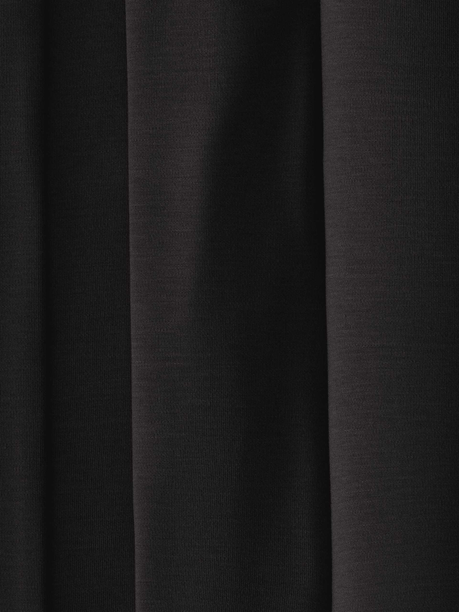 A close-up of dark, evenly folded fabric from the Women's Bedtime Bundle by Cozy Earth, with deep shadows and a smooth texture. The image shows parallel vertical lines formed by the folds, creating an elegant and understated appearance. |Color:Black