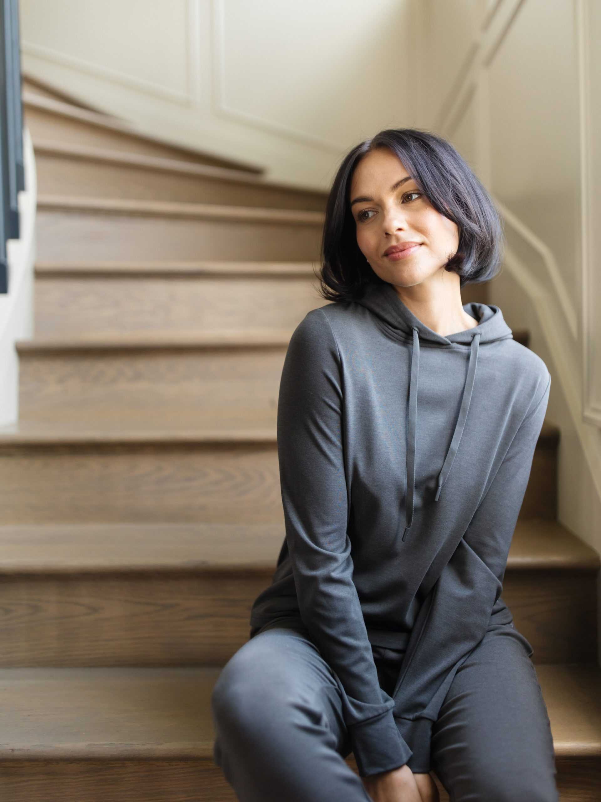 A woman sitting on stairs wearing a grey Cozy Earth Brushed Bamboo Hoodie with a drawstring and sleeve cuffs. |Color:Charcoal