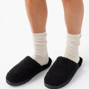 Close-up of a person's lower legs wearing white crew socks and Cozy Earth's Puffy Sheep Slipper, which are black and fuzzy. The background is plain white. |Color:Black Sheep
