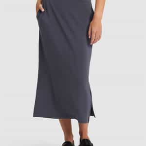A person is wearing the Cozy Earth Women's Brushed Bamboo Midi Skirt in dark gray, featuring a high waist, side pockets, and small side slits, paired with black loafers. The upper body and face are not visible.|Color:Graphite
